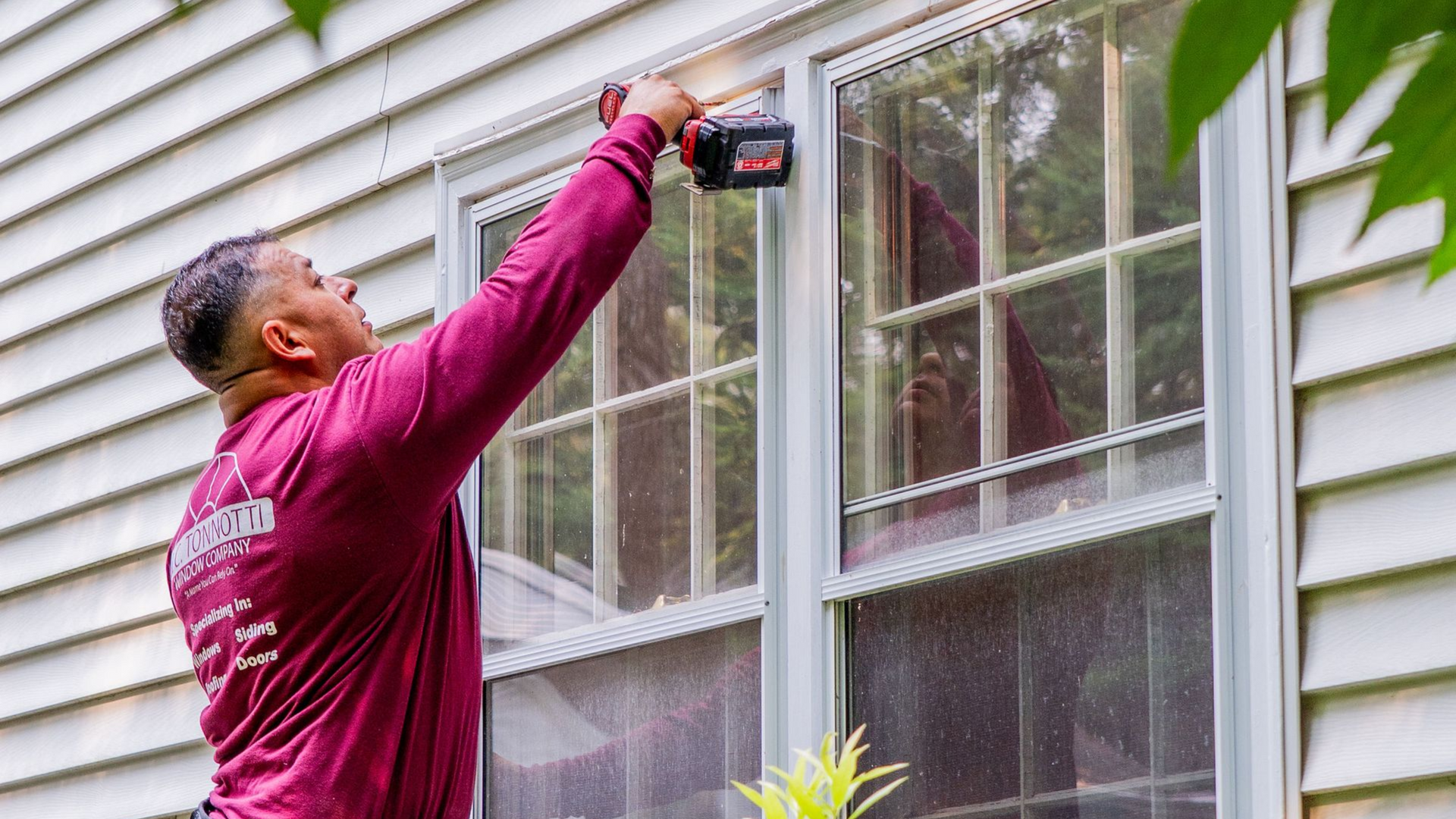 Person using a power drill to work on a window of a white house.