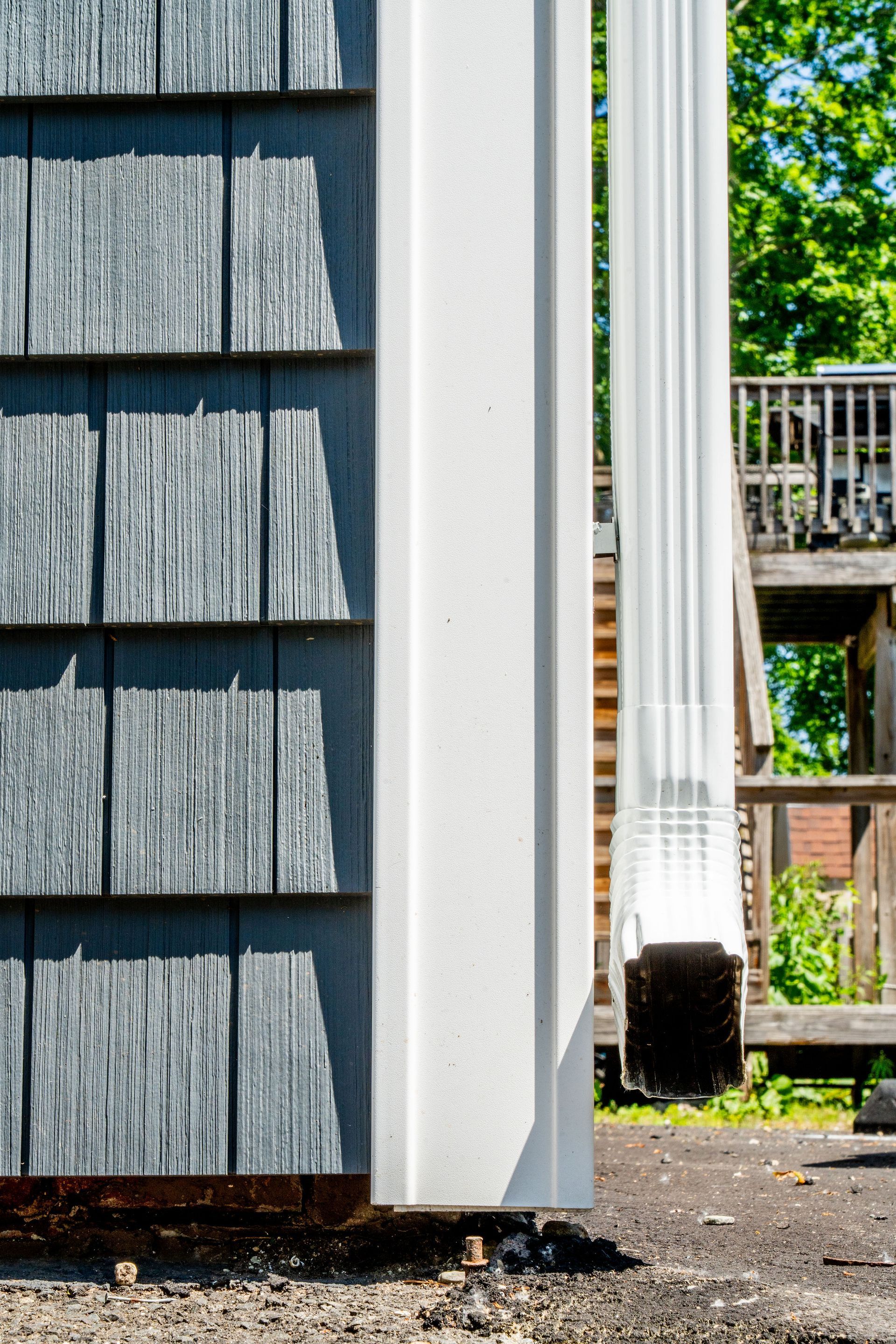 Blue wooden siding beside a white post and gutter. Outdoors, sunny, and near a deck.