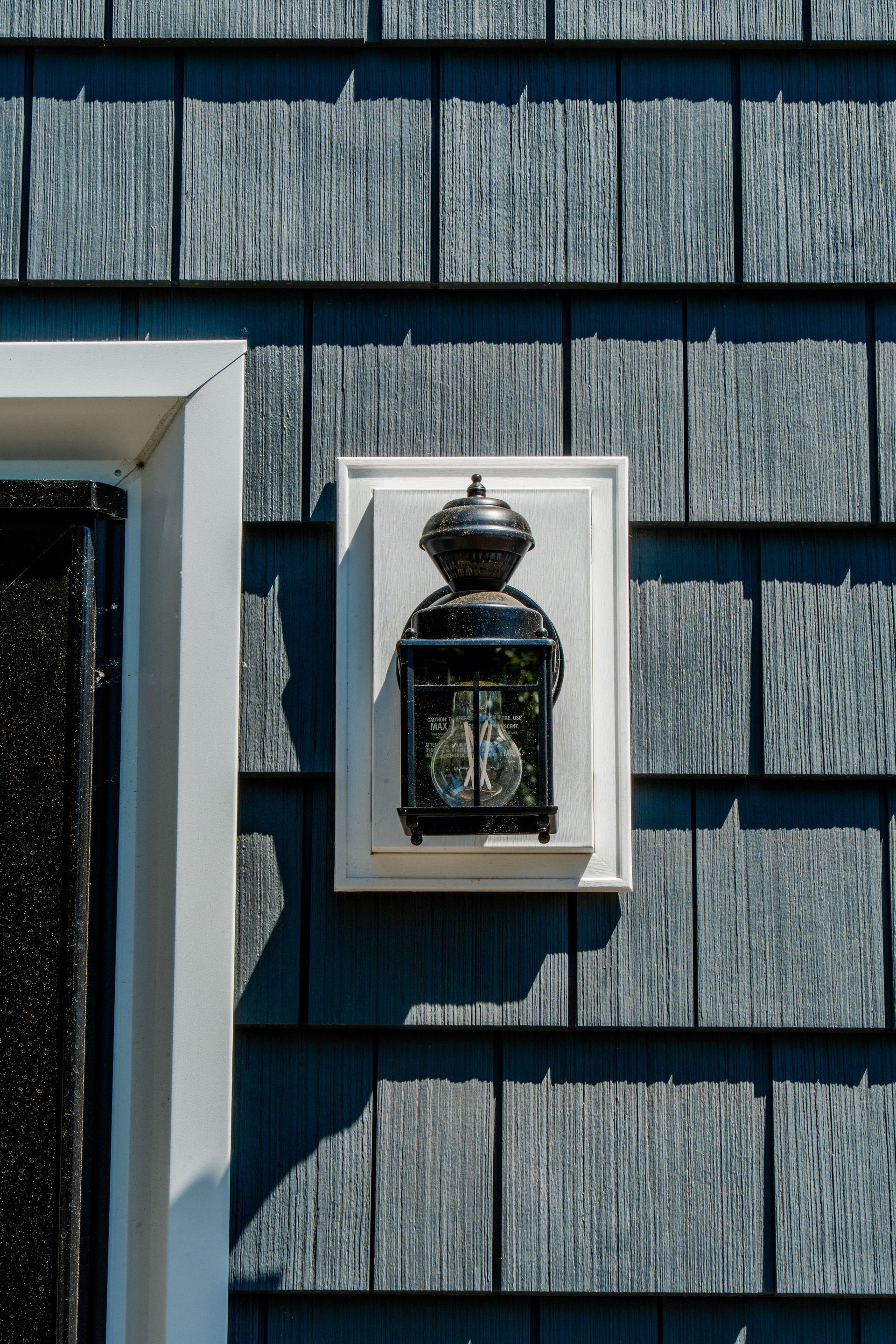 Lantern on gray shingle siding, framed by white trim.
