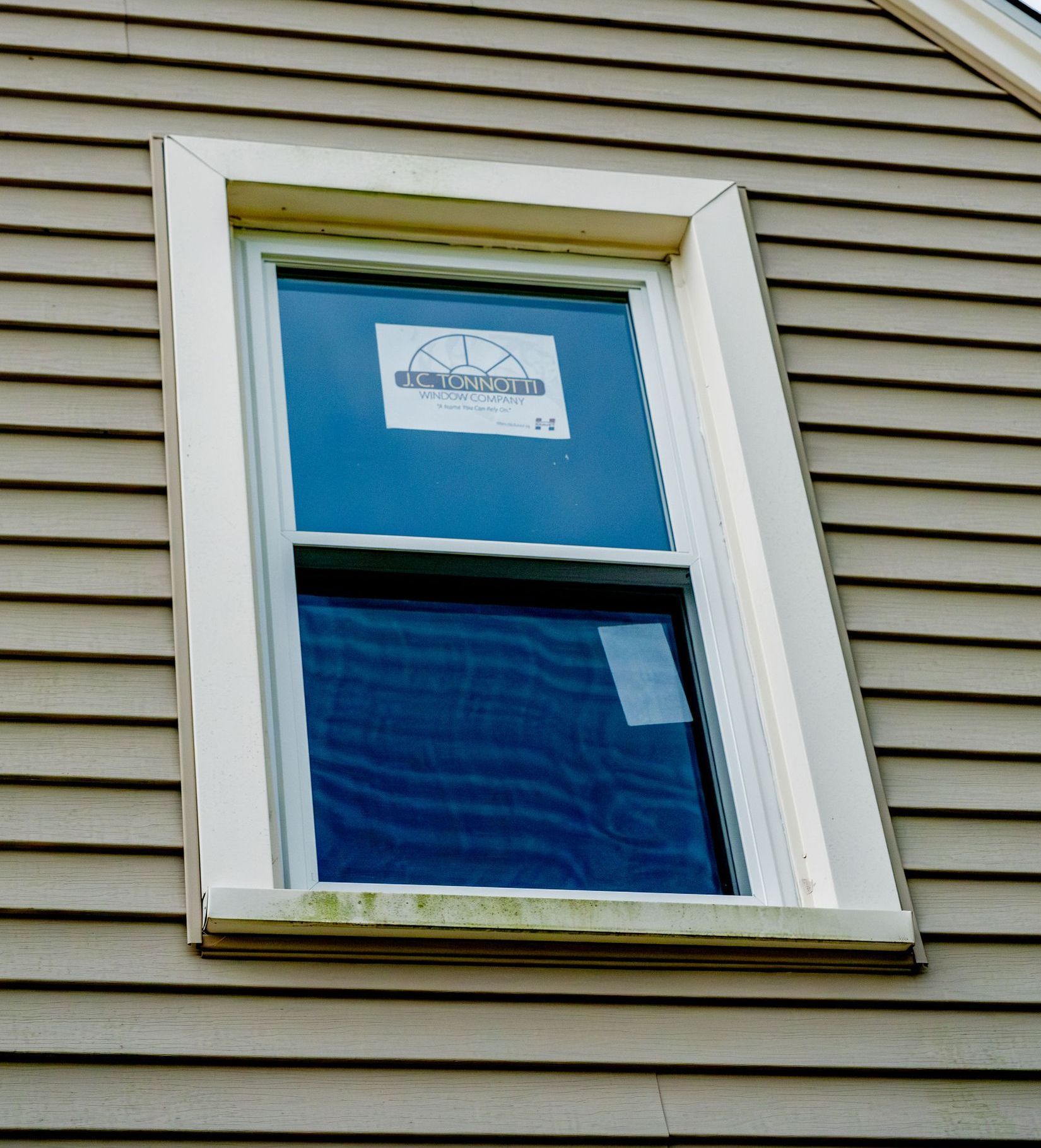 A double hung window on the side of a house has a sticker on it that says jc tonnotti