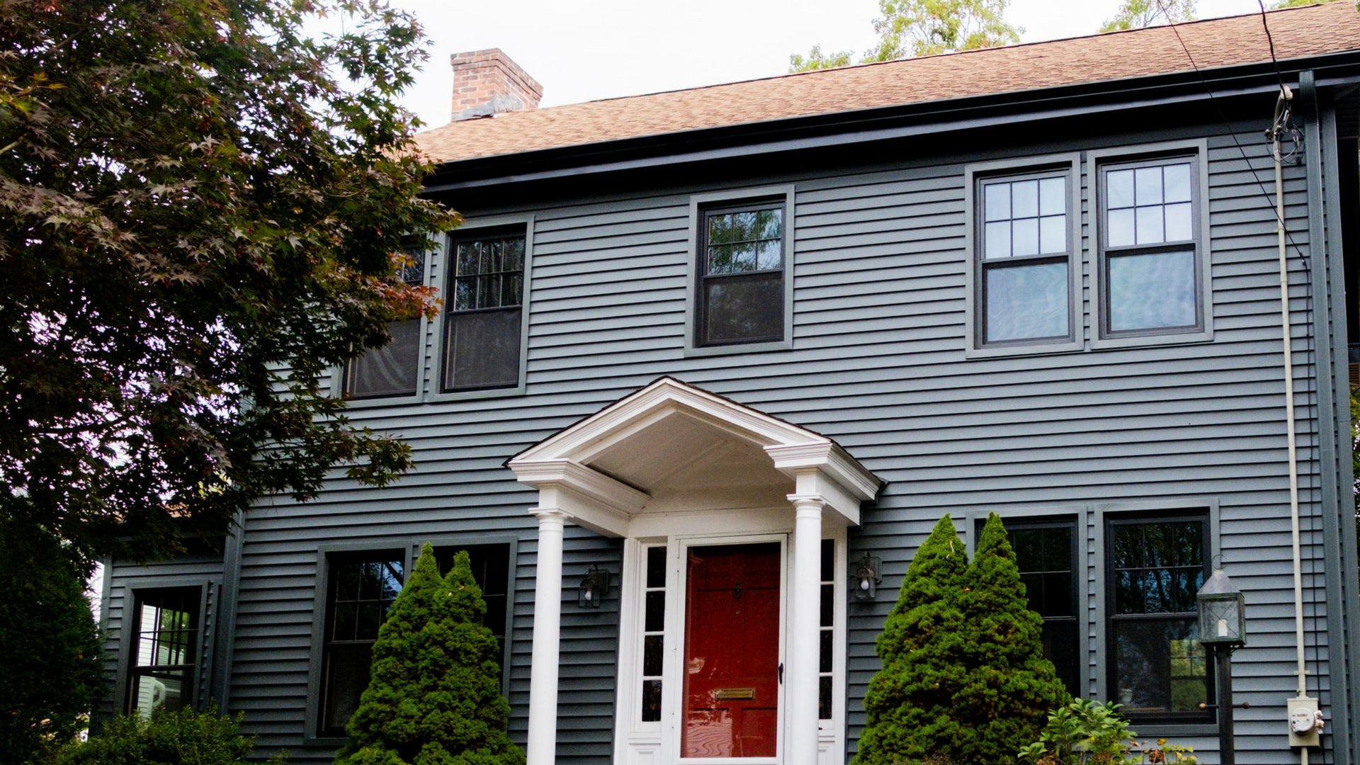 Two-story gray clapboard house with red door, white trim, and small porch.