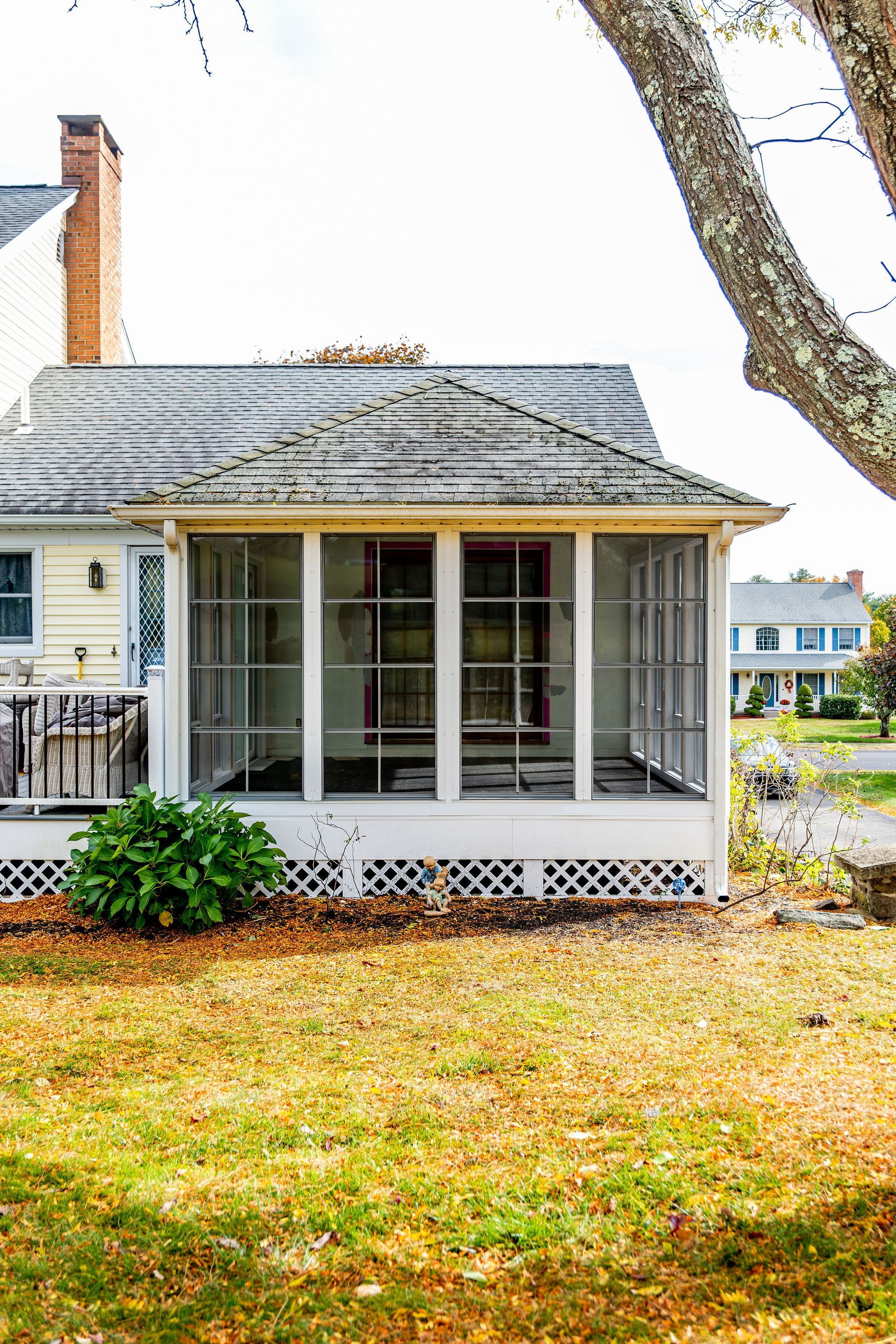 Screened-in porch with white trim, yellow house, and brown grass. A tree trunk is on the right.