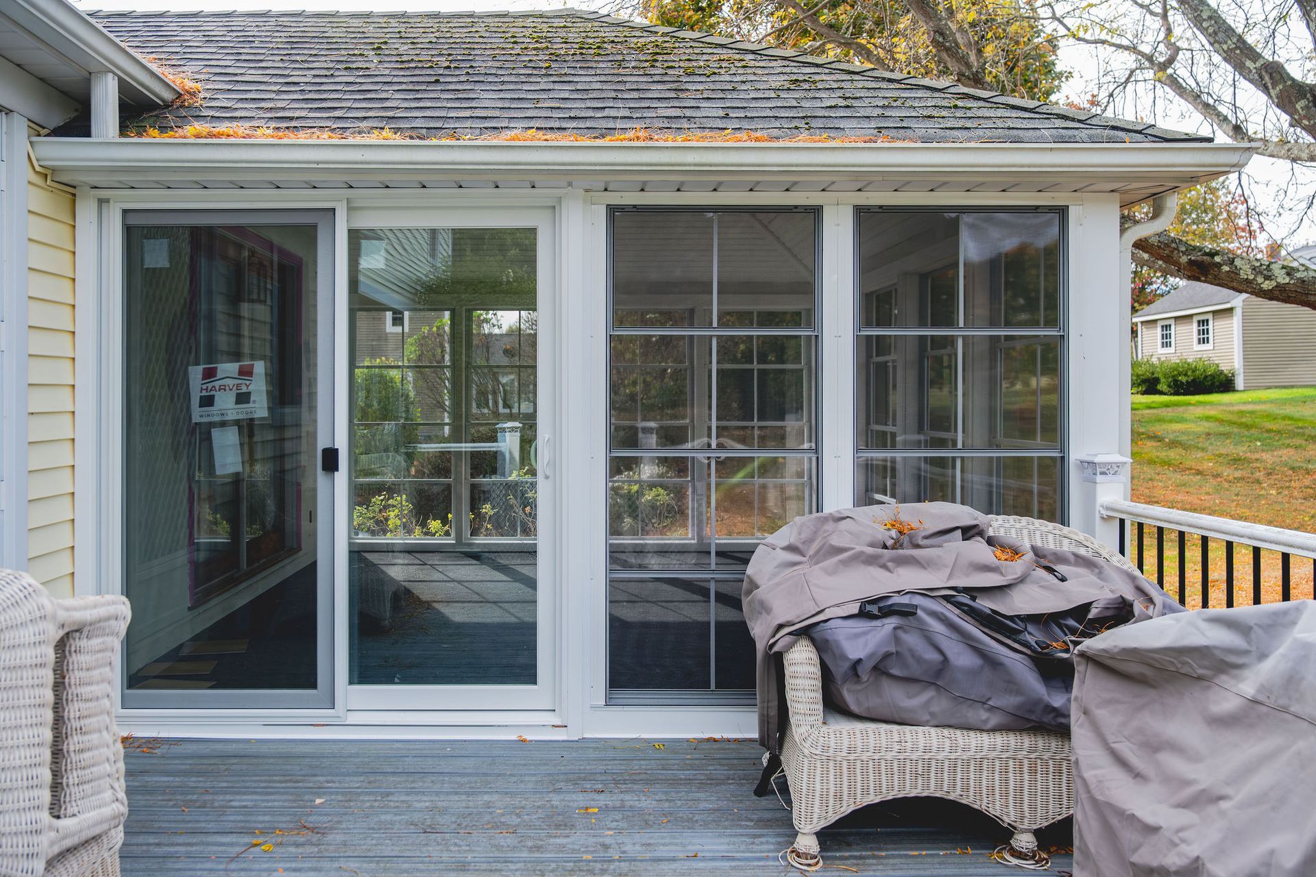 Screened porch with sliding glass door, wicker chair, and barbecue grill covered by a tarp.