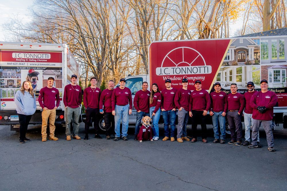 Group photo of J.C. Tonnotto Window & Door team in maroon shirts, posing in front of their trucks.