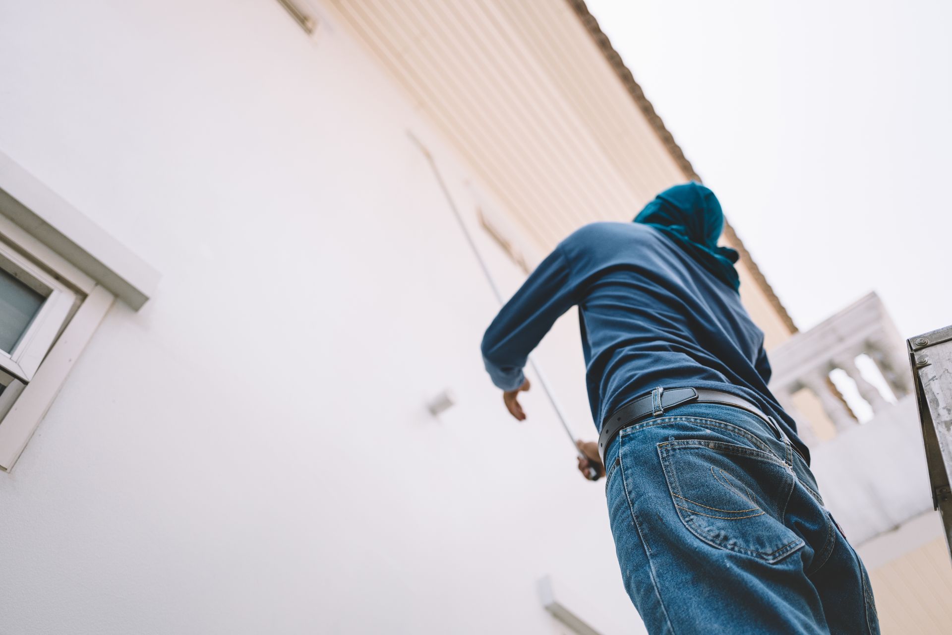Person in blue hoodie and jeans running alongside a white building, viewed from below