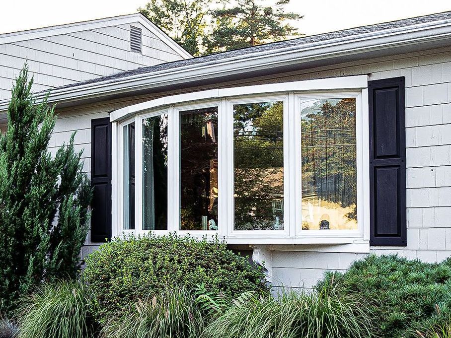 A white house with a large bay window and black shutters.