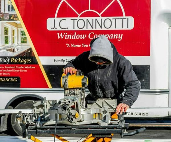 A man is working on a saw in front of a j.c. tonnotti window company truck