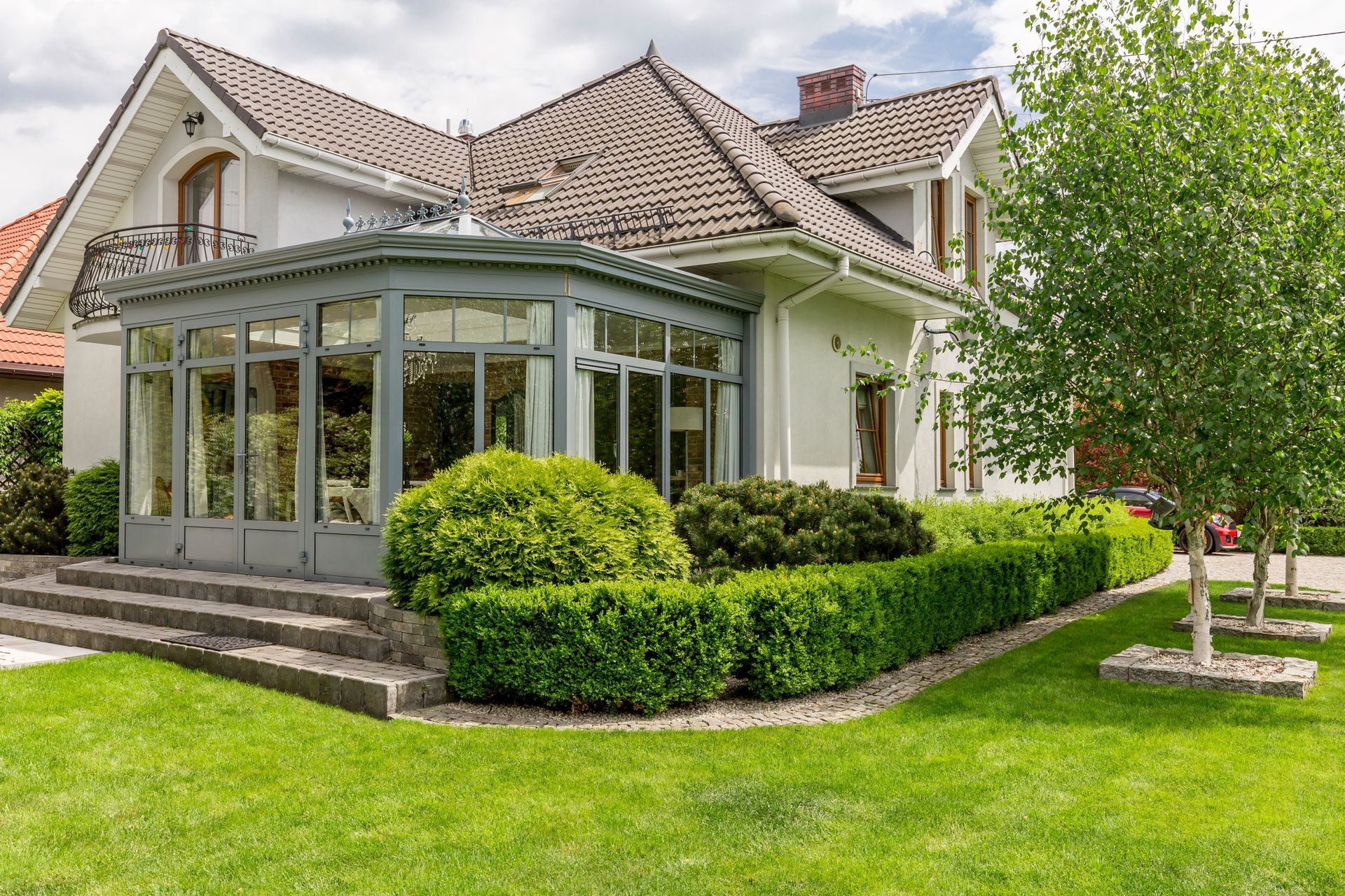 Gray house with glass sunroom, manicured hedges, and a green lawn