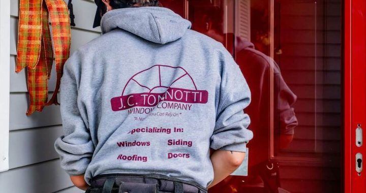 A man wearing a hoodie that says jc to notti is standing in front of a red door.