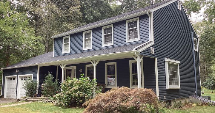 A large blue house with white trim is surrounded by trees.