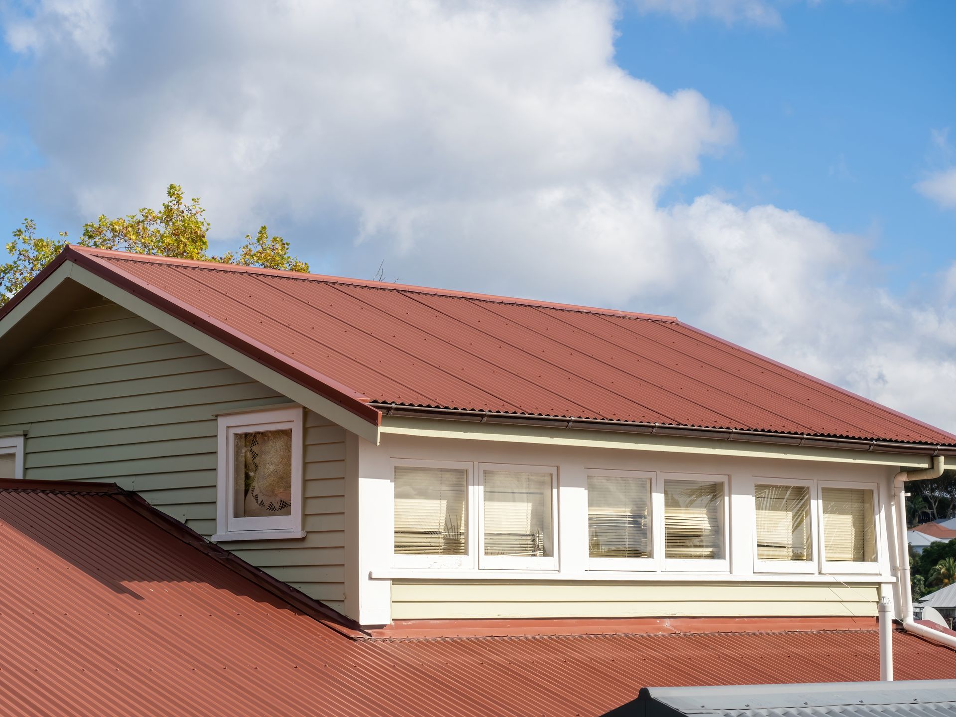 Red metal roof on a house with beige siding and blue sky with clouds above