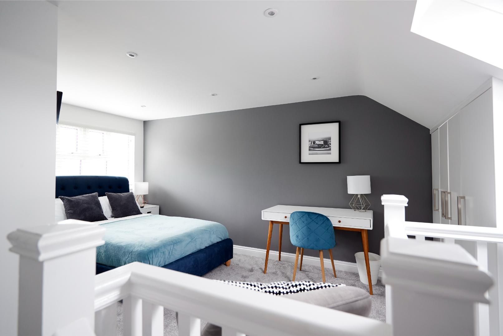 Bedroom with a bed, desk, and chair; gray walls, white railing, skylight.
