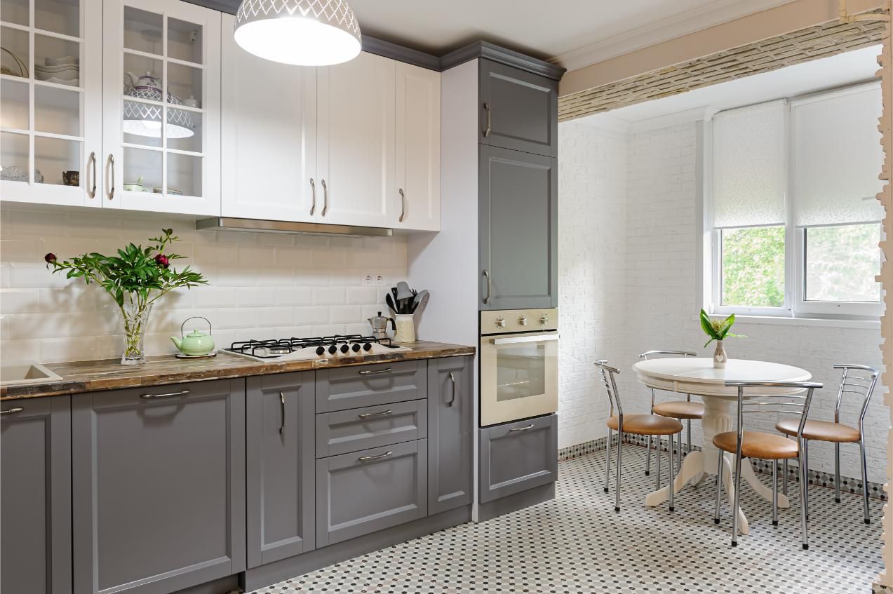 Gray and white kitchen with cabinets, stove, oven, round table, and chairs.