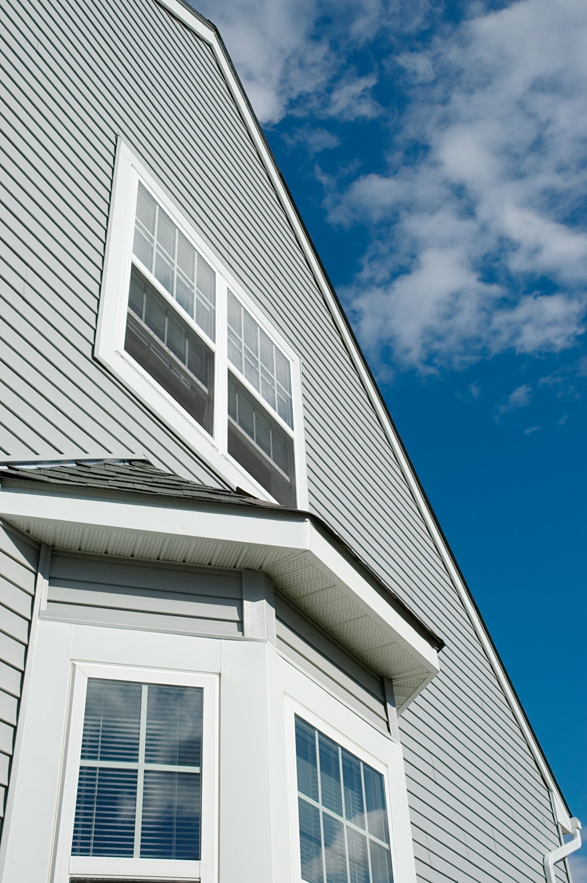 White house siding and windows against a blue sky with clouds