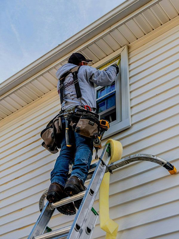 A man is standing on a ladder fixing a window on the side of a house.