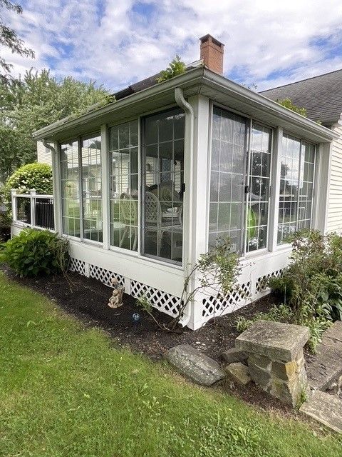 A sun room with a lot of windows and chairs in the backyard of a house.