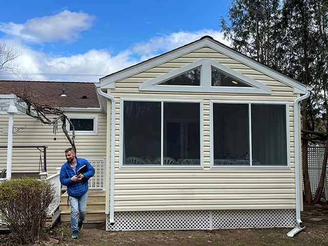 A man is standing in front of a house with a screened in porch.