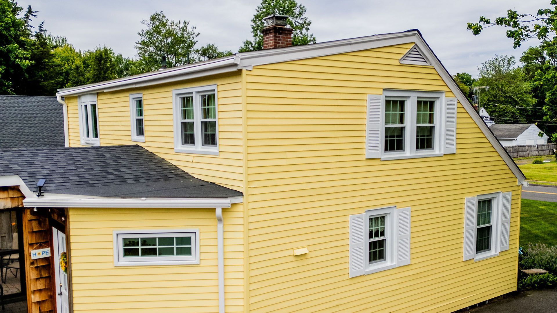 A yellow house with white shutters and a black roof.