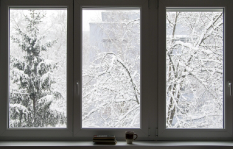 Three windows with snow on the trees and a cup on the window sill.