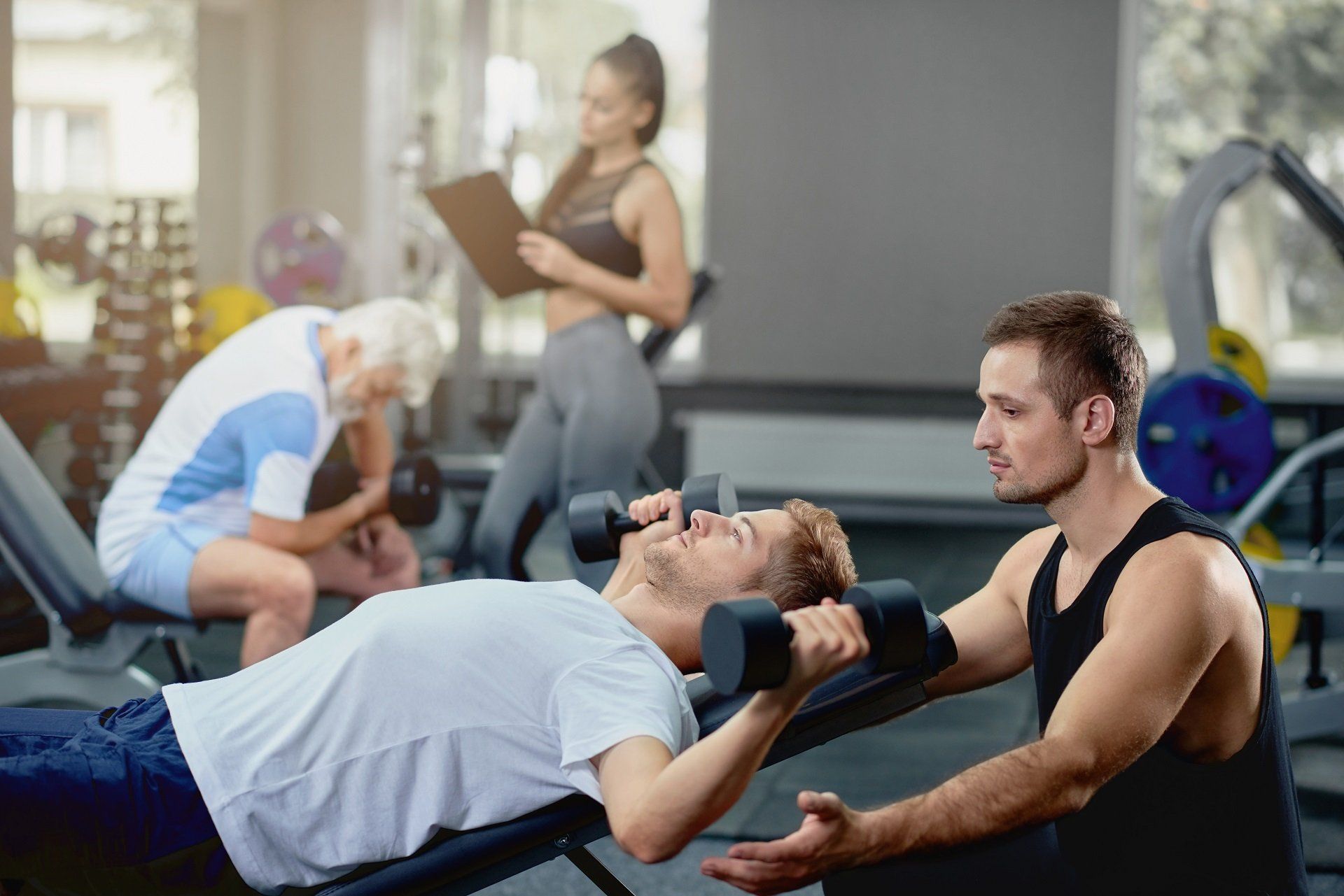 A man is lifting a dumbbell on a bench in a gym.