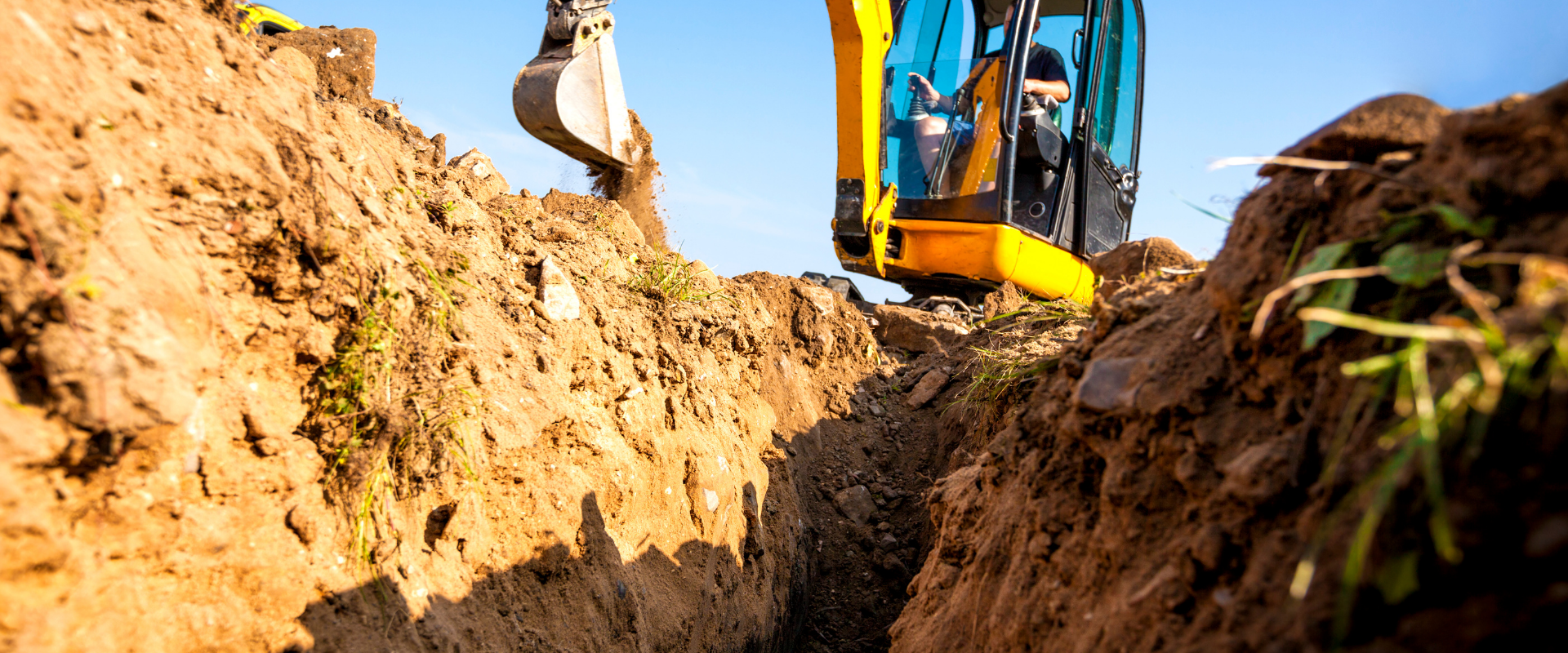 A yellow excavator is digging a trench in the dirt.