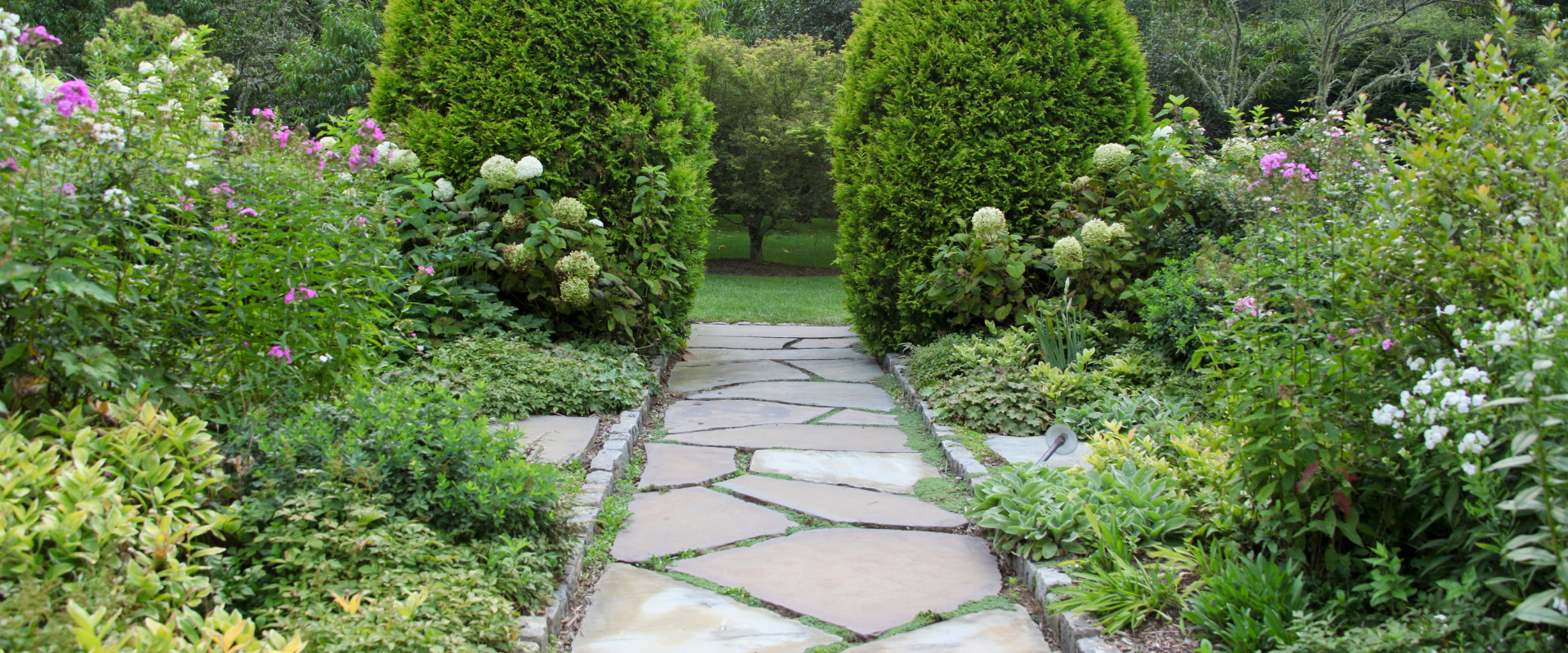 A stone path in a garden surrounded by trees and flowers.