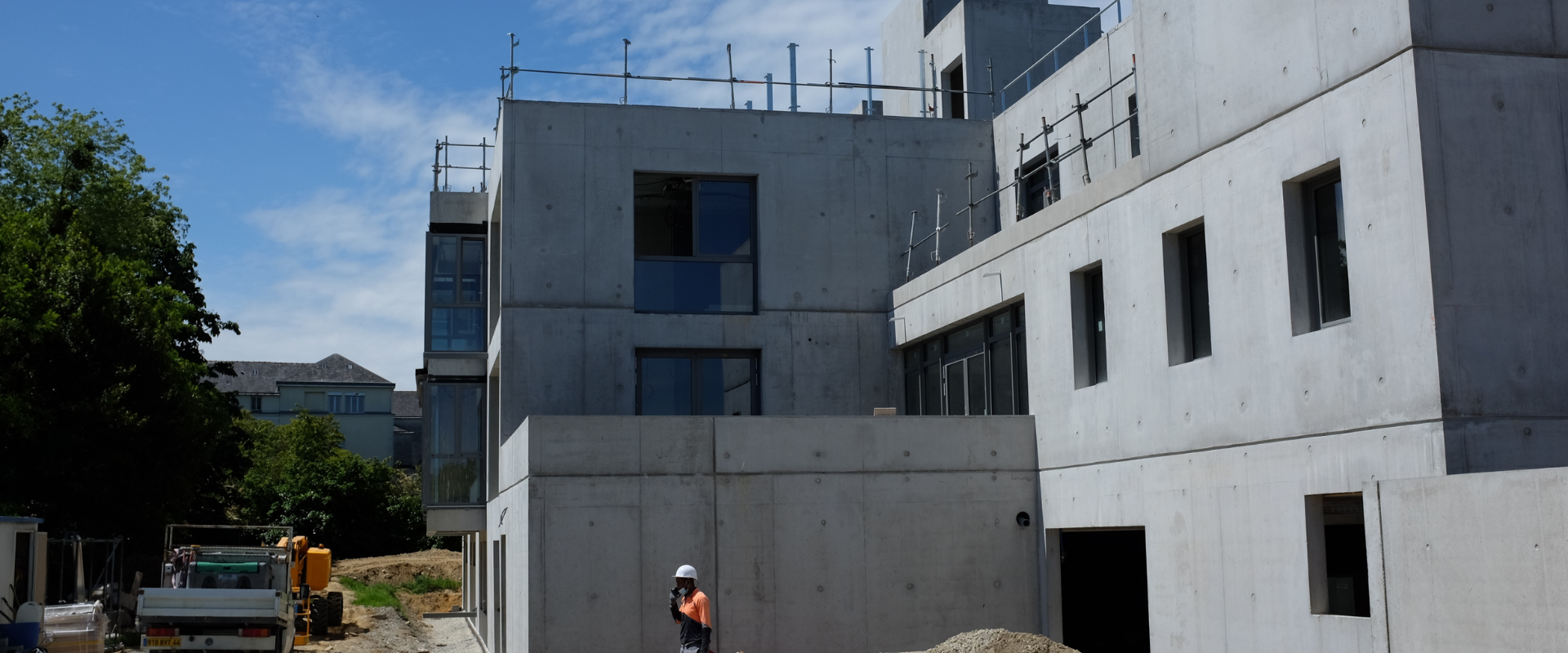 A man is standing in front of a large concrete building under construction.