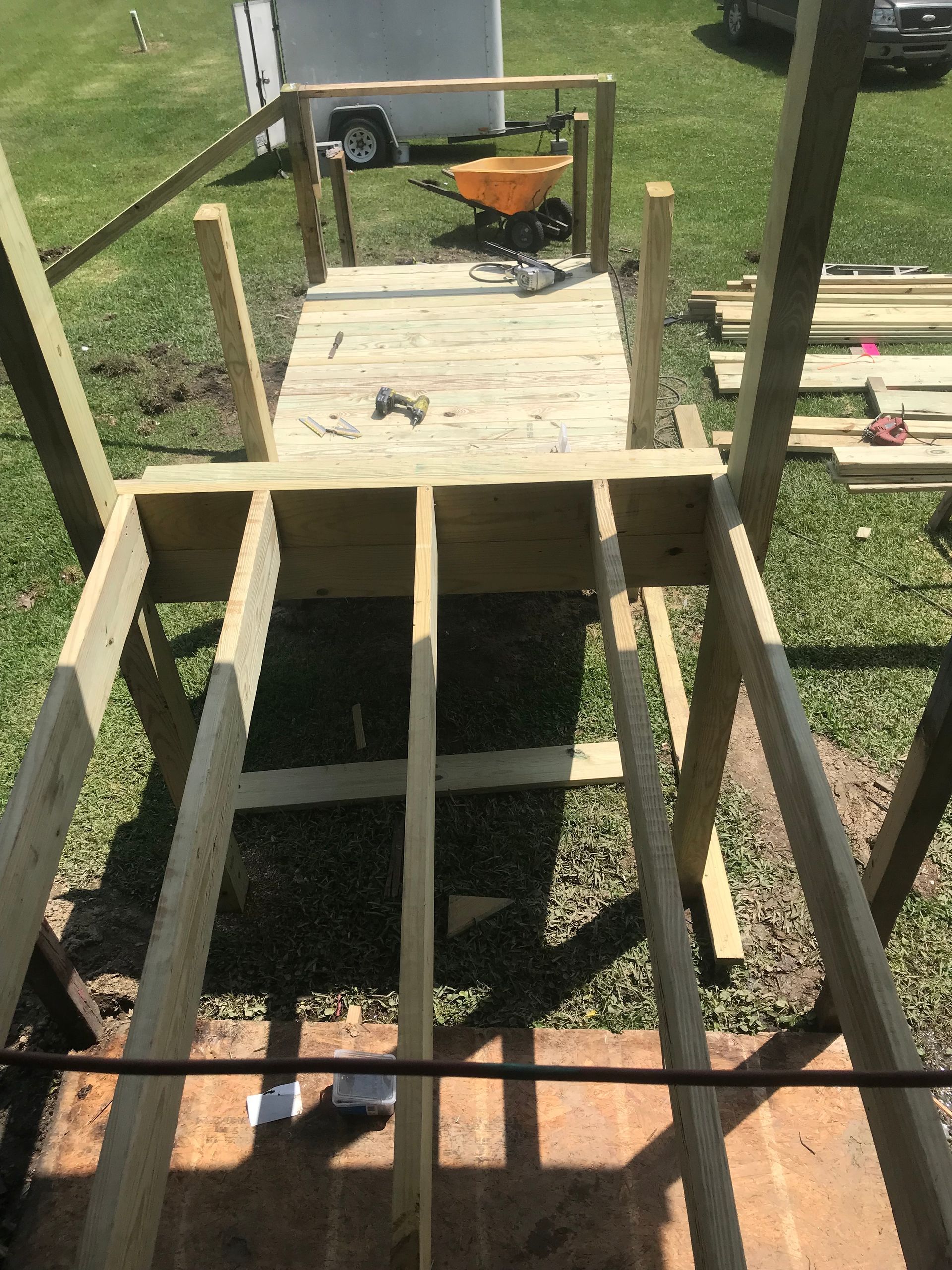 A wooden structure is being built in the grass with a wheelbarrow in the background.