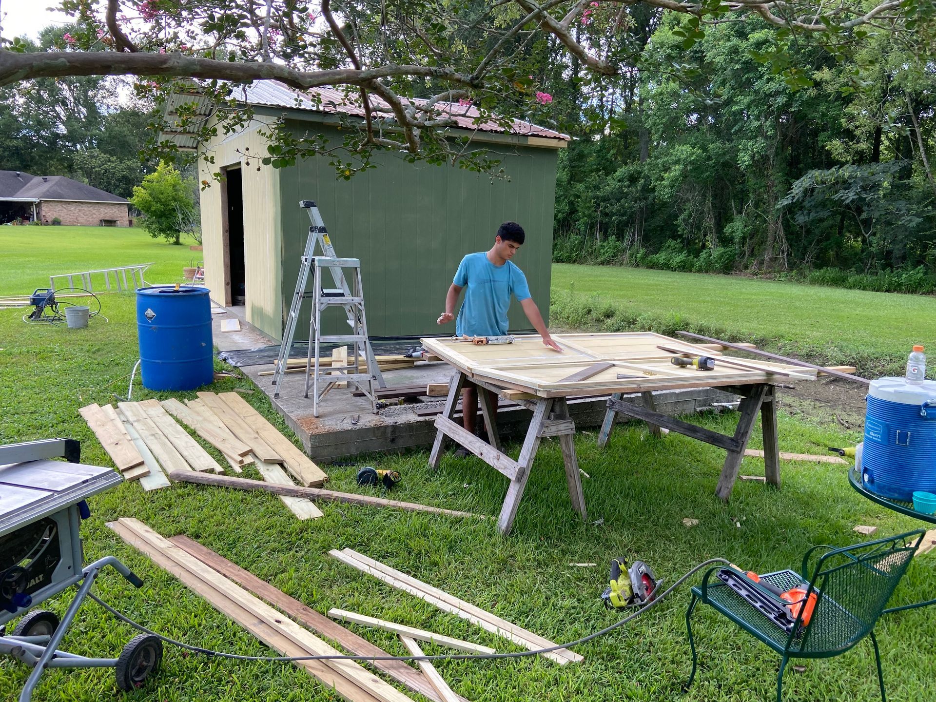 A man is standing at a table in the grass cutting wood.