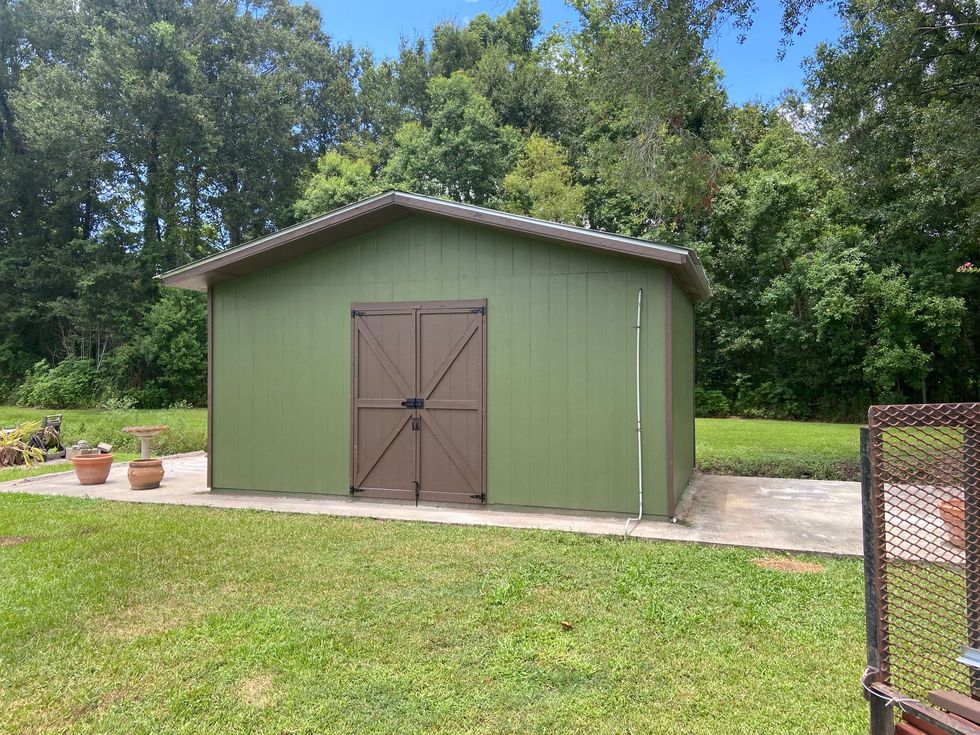 A green shed with brown doors is sitting in the middle of a lush green field.