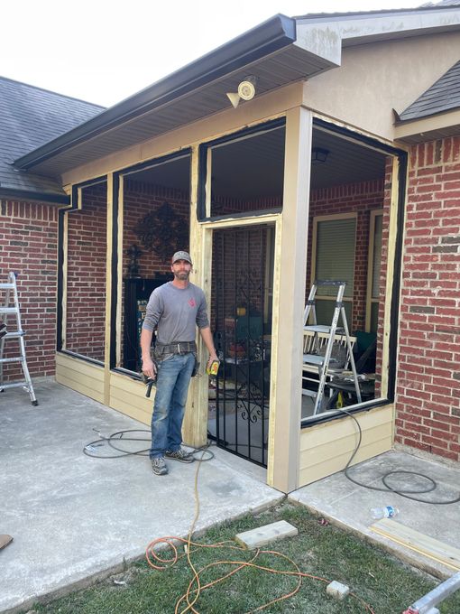 A man is standing in front of a screened in porch being built on a brick house.