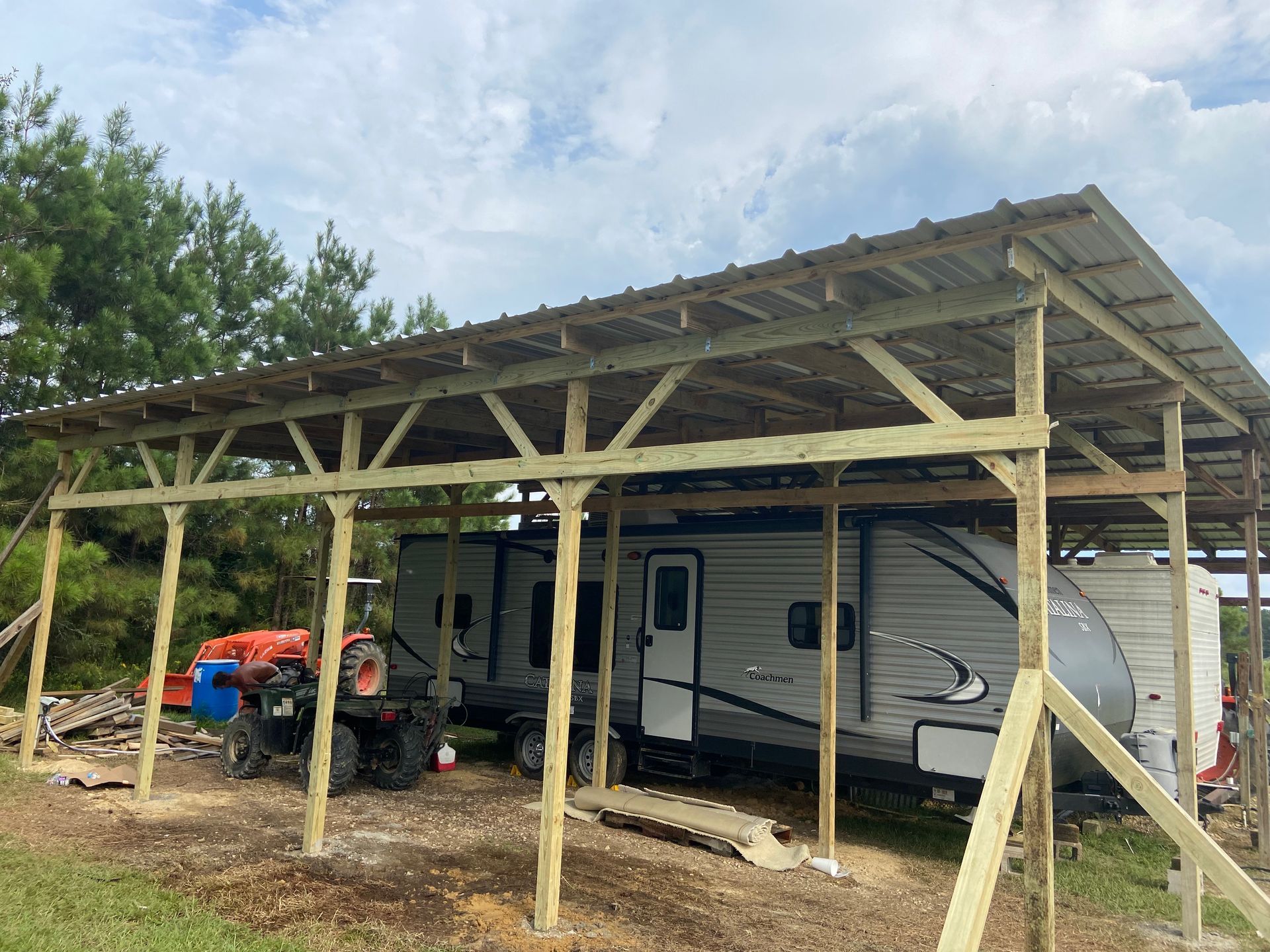 A trailer is parked under a wooden structure.