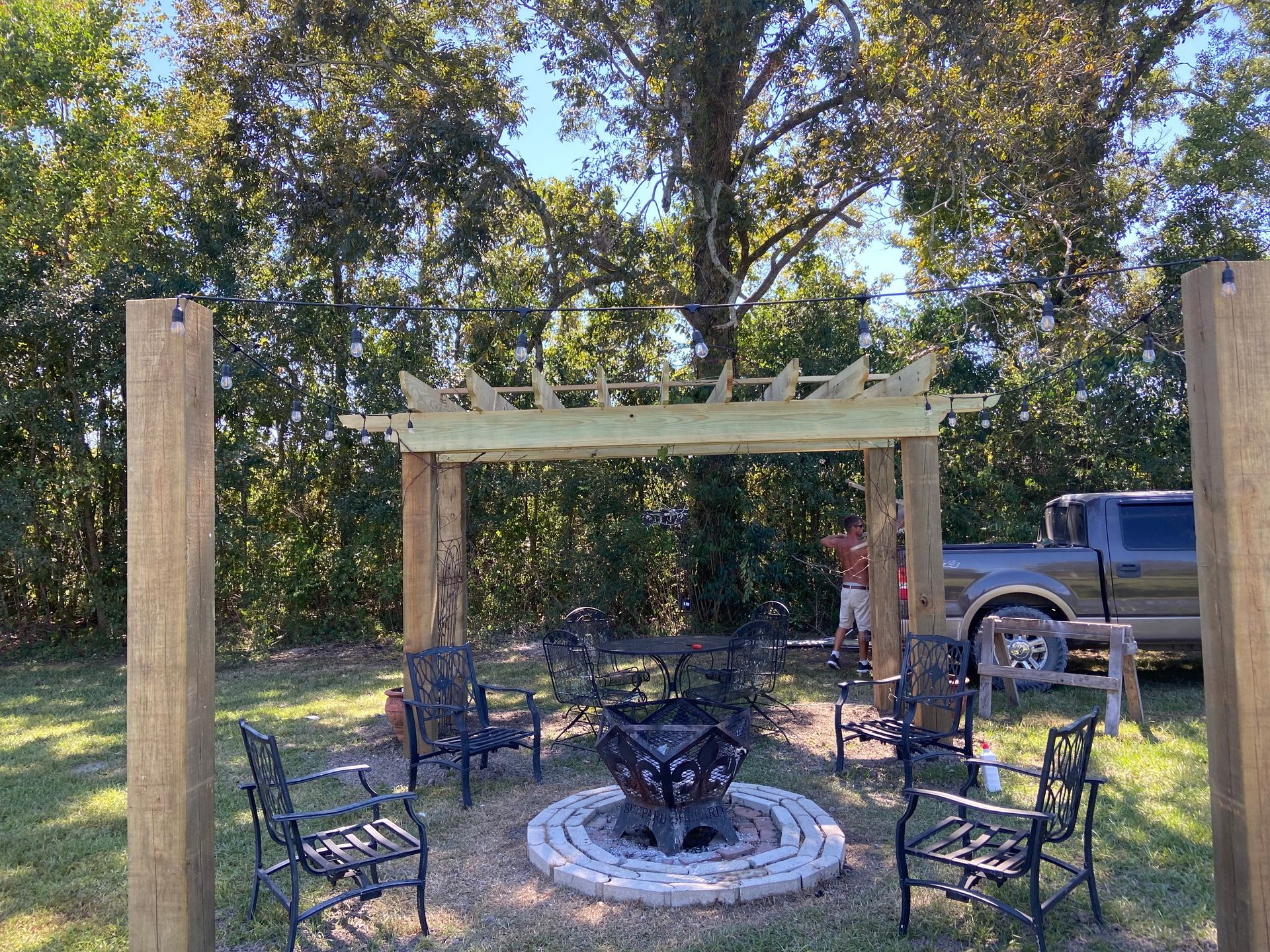 A fire pit is surrounded by chairs and a pergola.