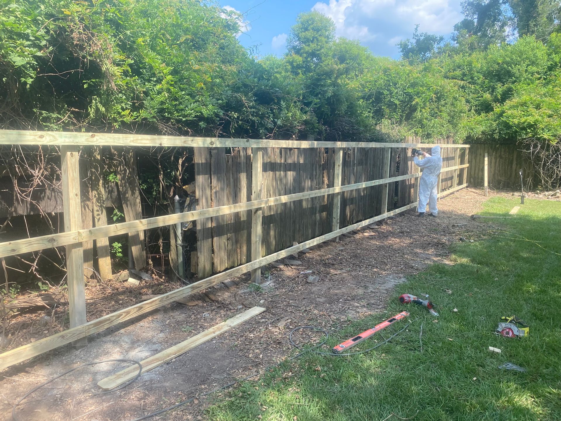 A man is standing next to a wooden fence in a yard.