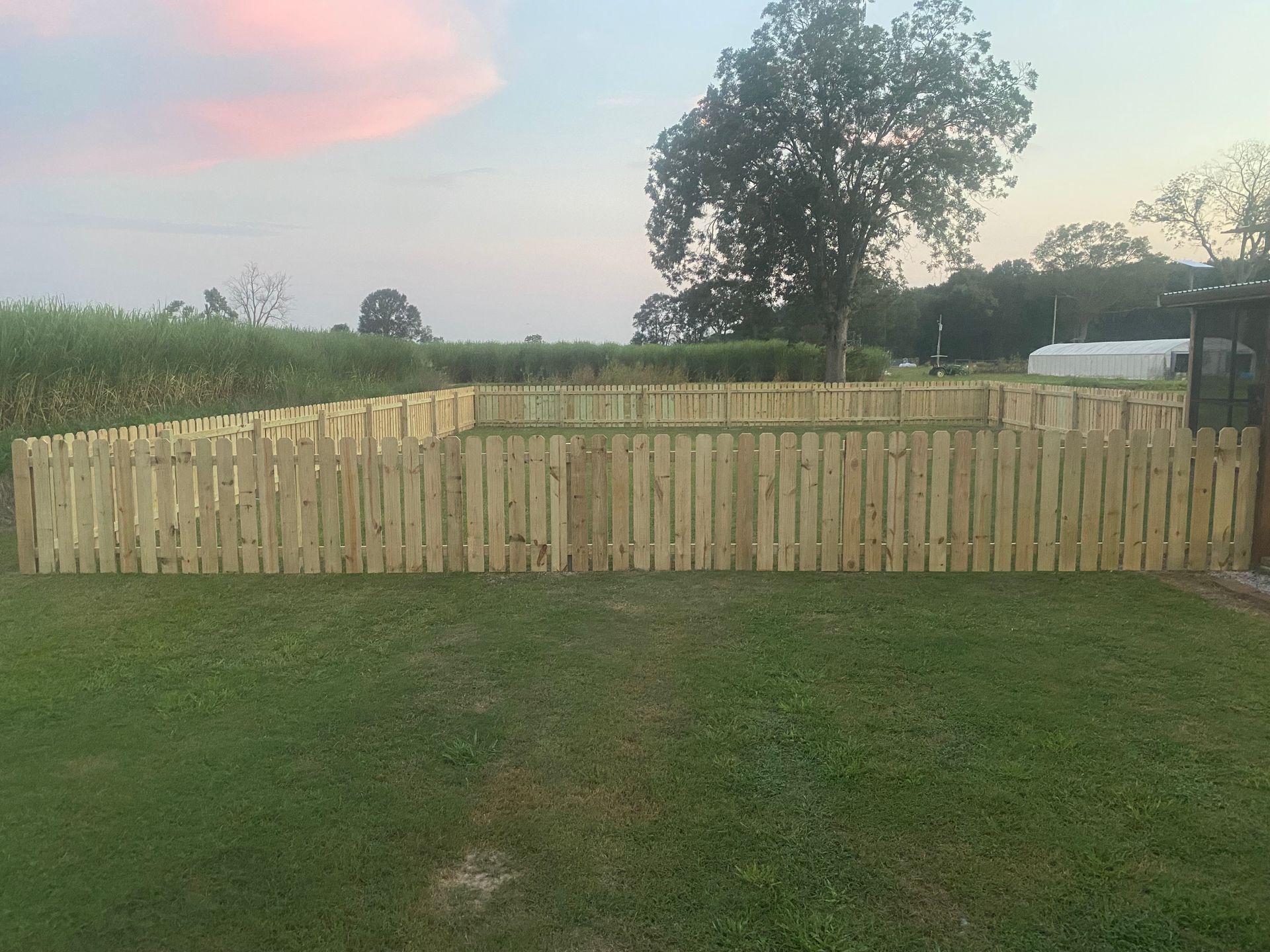 A wooden picket fence surrounds a lush green field.