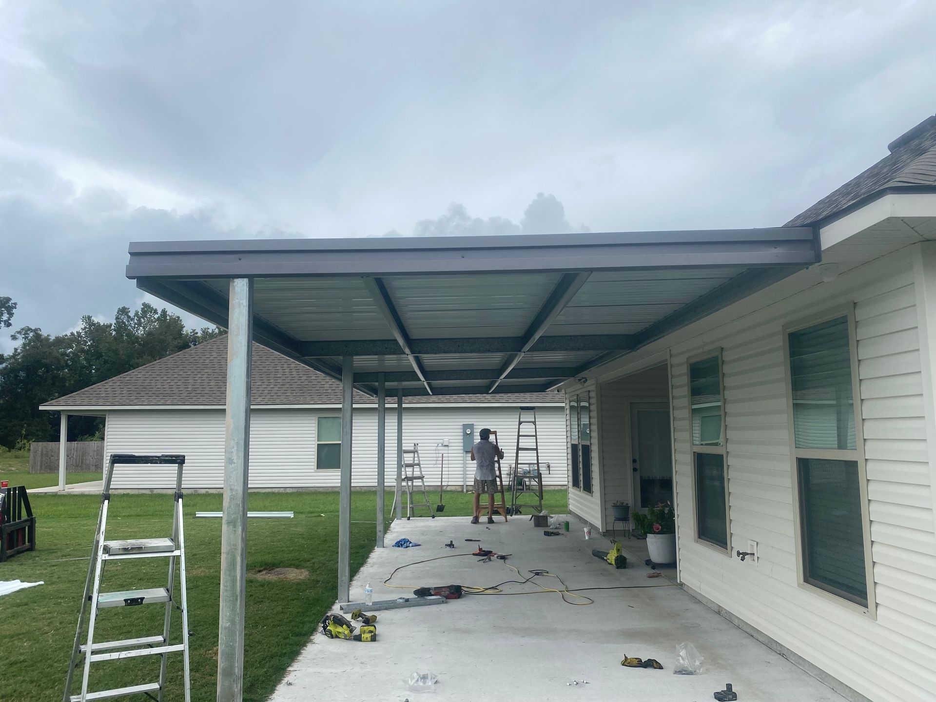 A man is standing under a covered patio in front of a house.