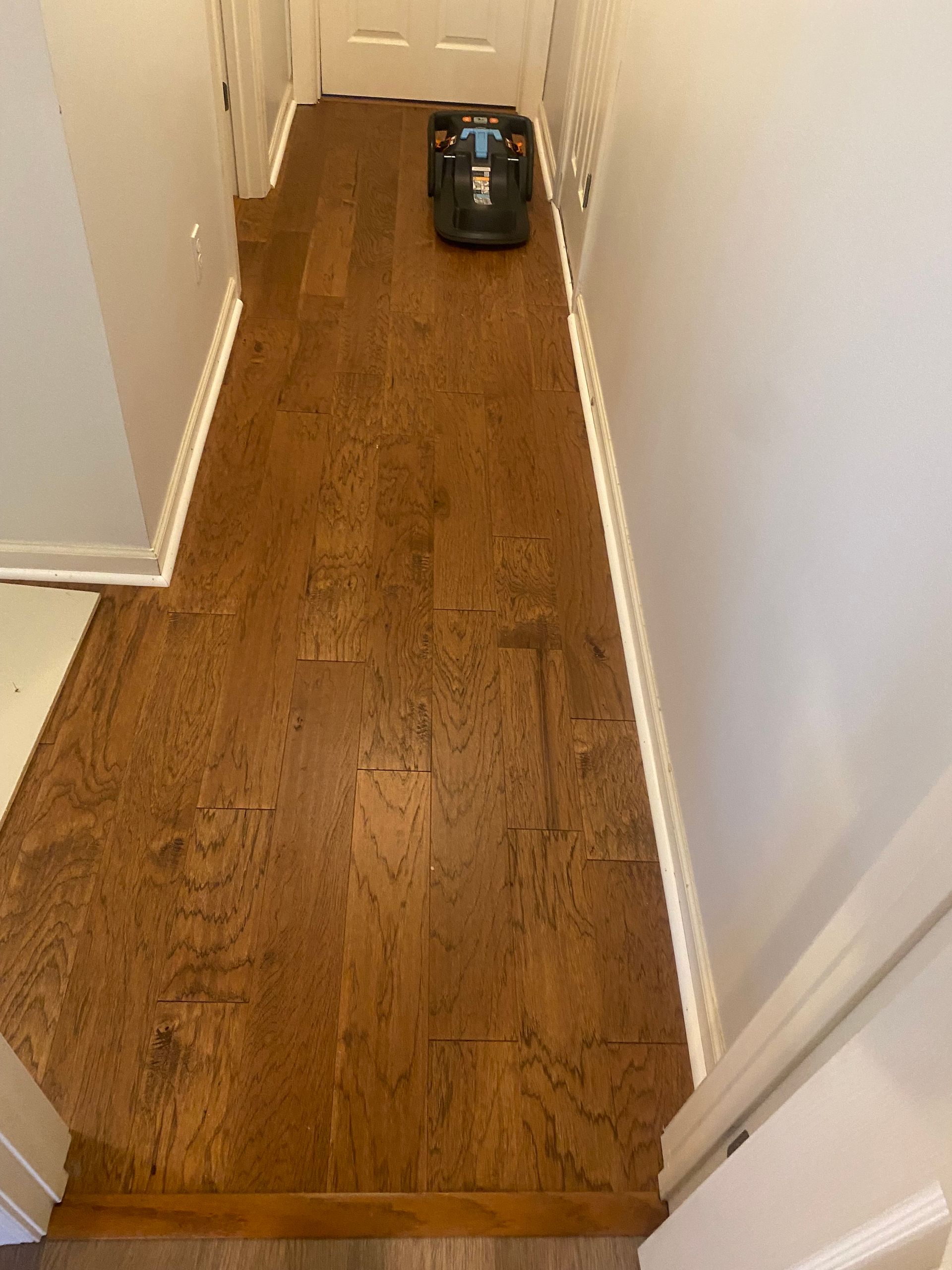 A robot vacuum cleaner is sitting on a wooden floor in a hallway.