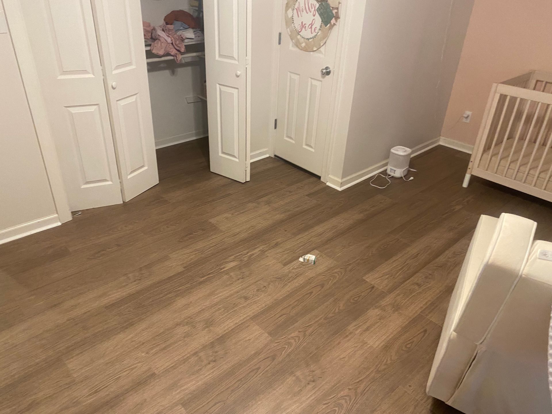 A bedroom with hardwood floors , a crib , and a closet.