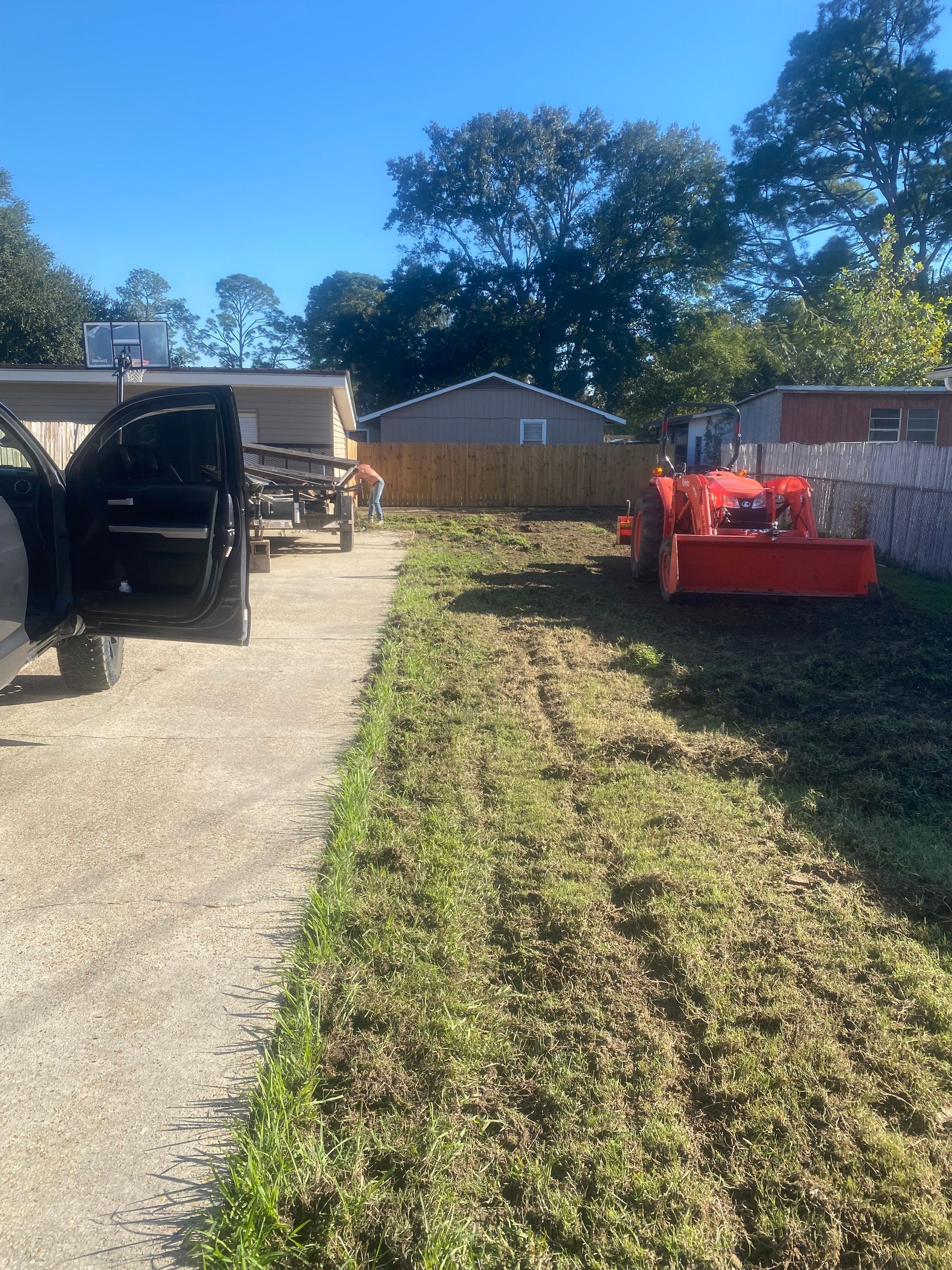 A tractor is cutting grass in a yard next to a truck.