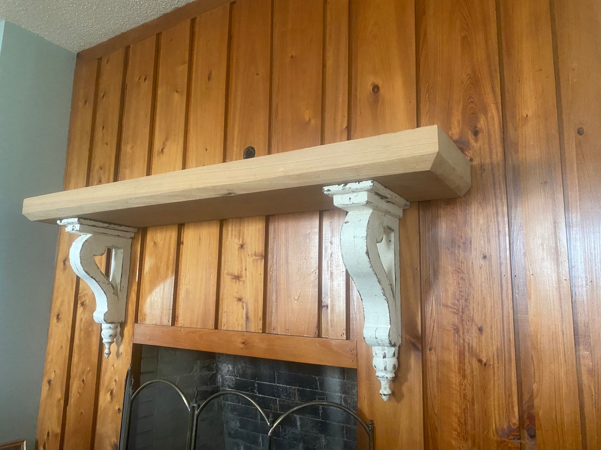 A wooden shelf is hanging over a fireplace with white brackets.