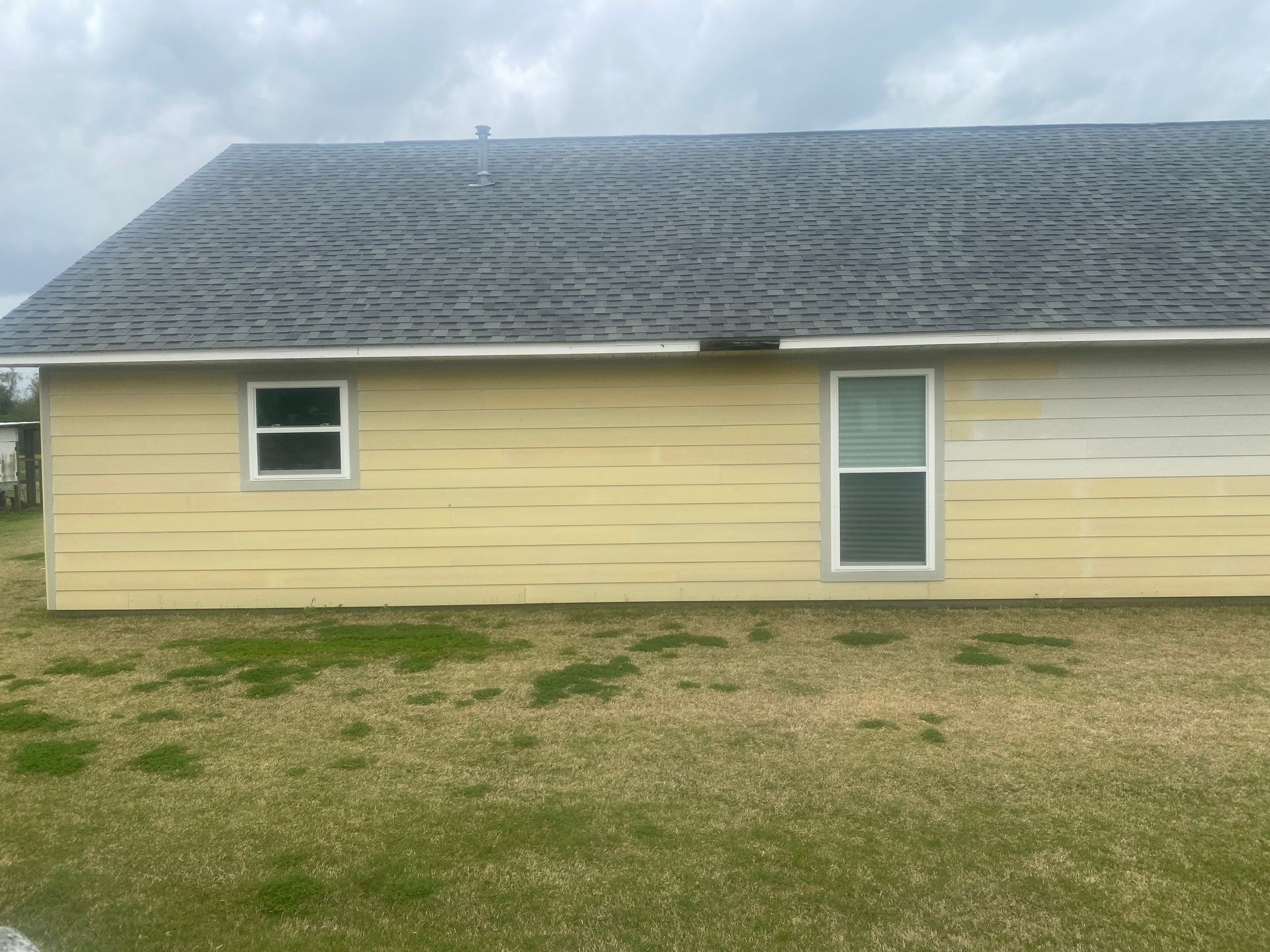 A house with a gray roof and yellow siding is sitting on top of a lush green field.