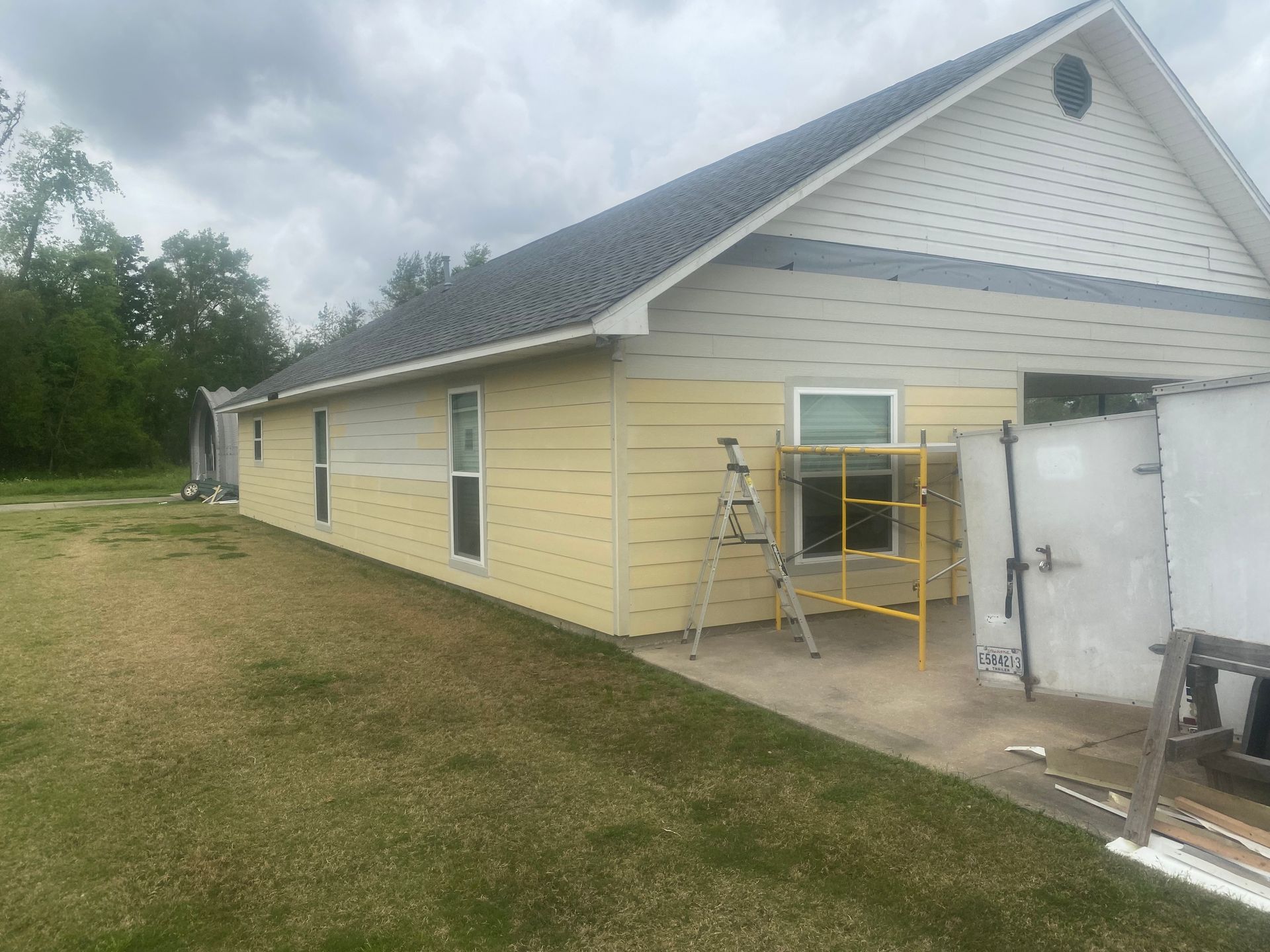 A house is being painted yellow and white with a ladder in front of it.