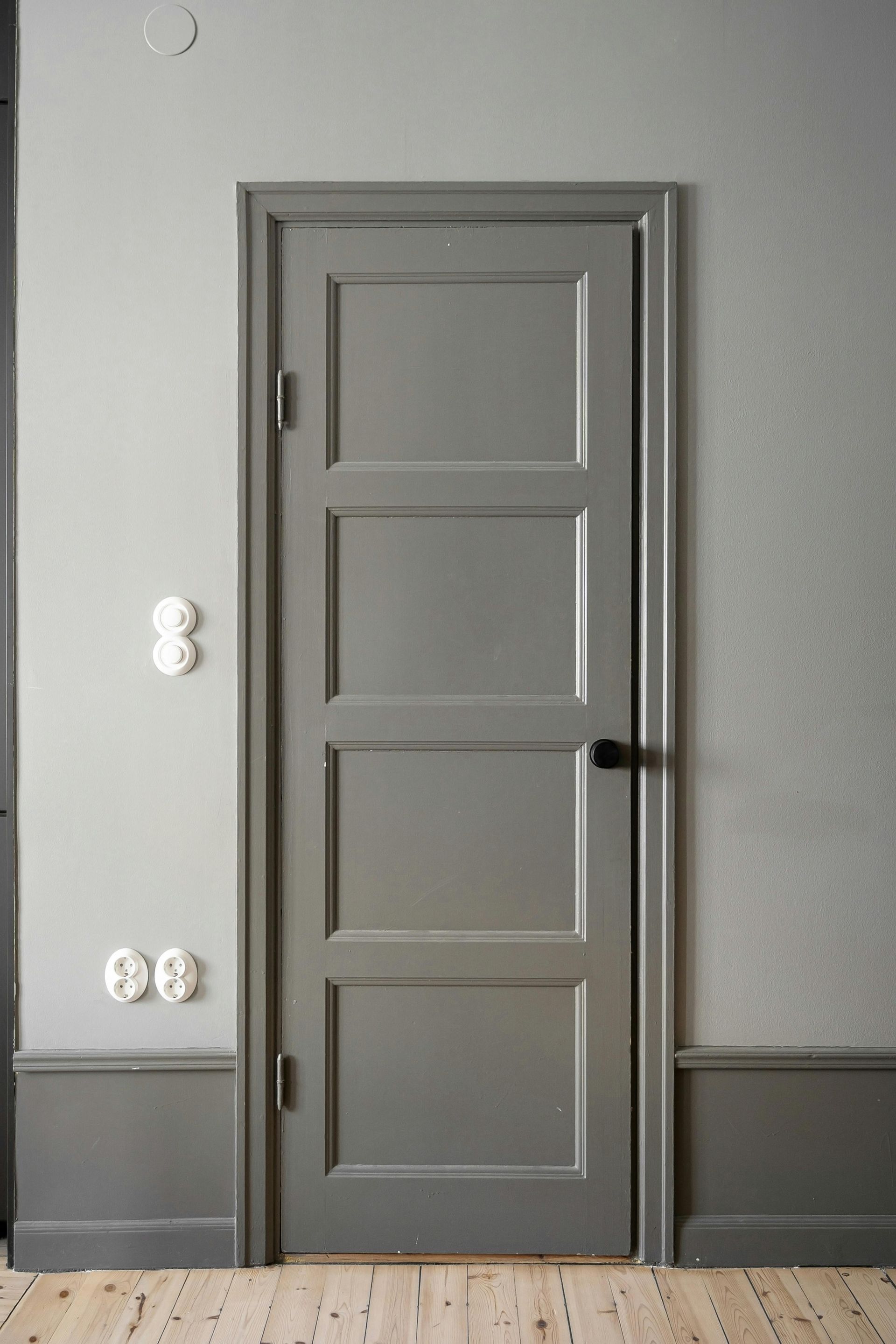 A gray door is in a room with gray walls and a wooden floor.