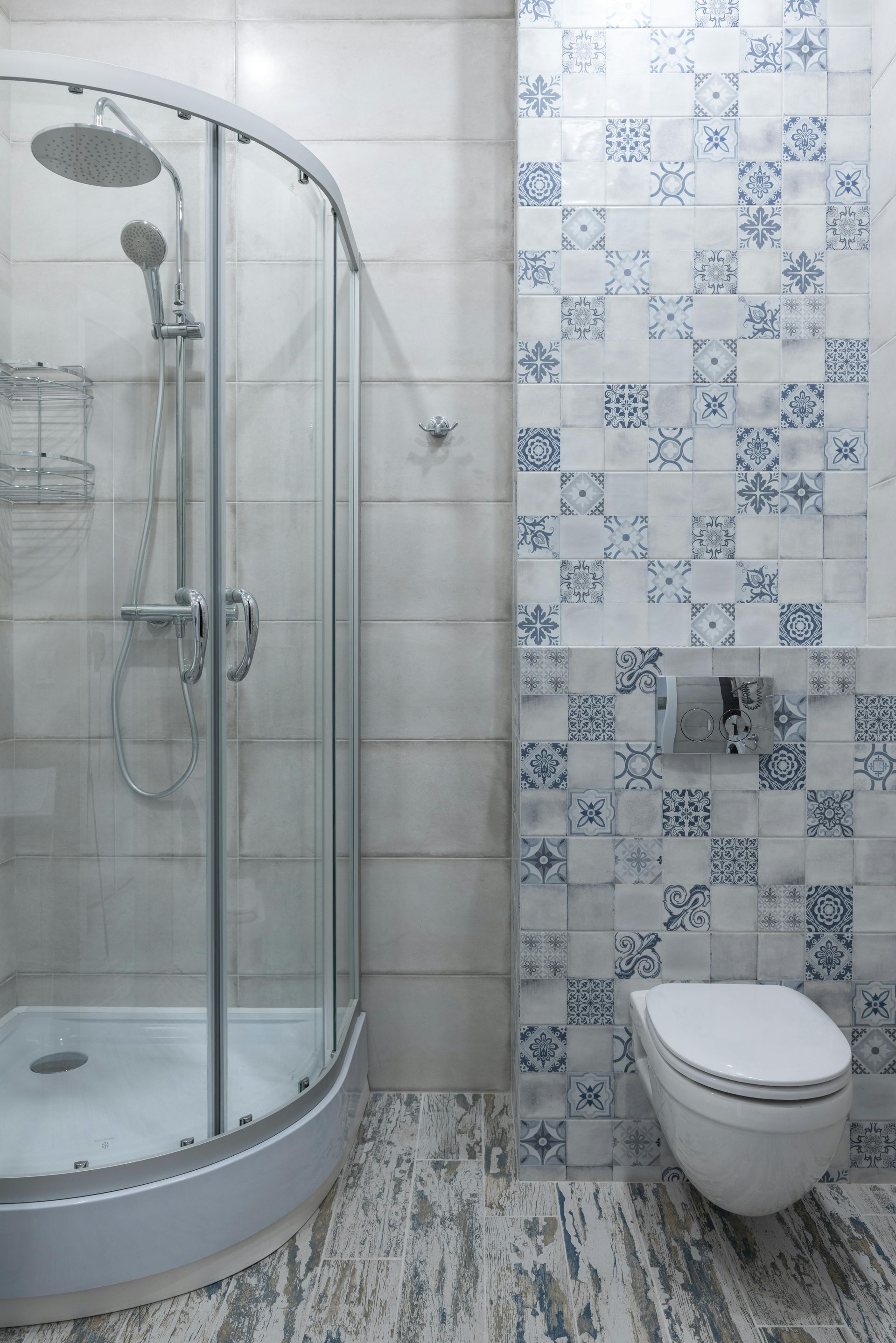 A bathroom with a shower stall , toilet and blue and white tiles.