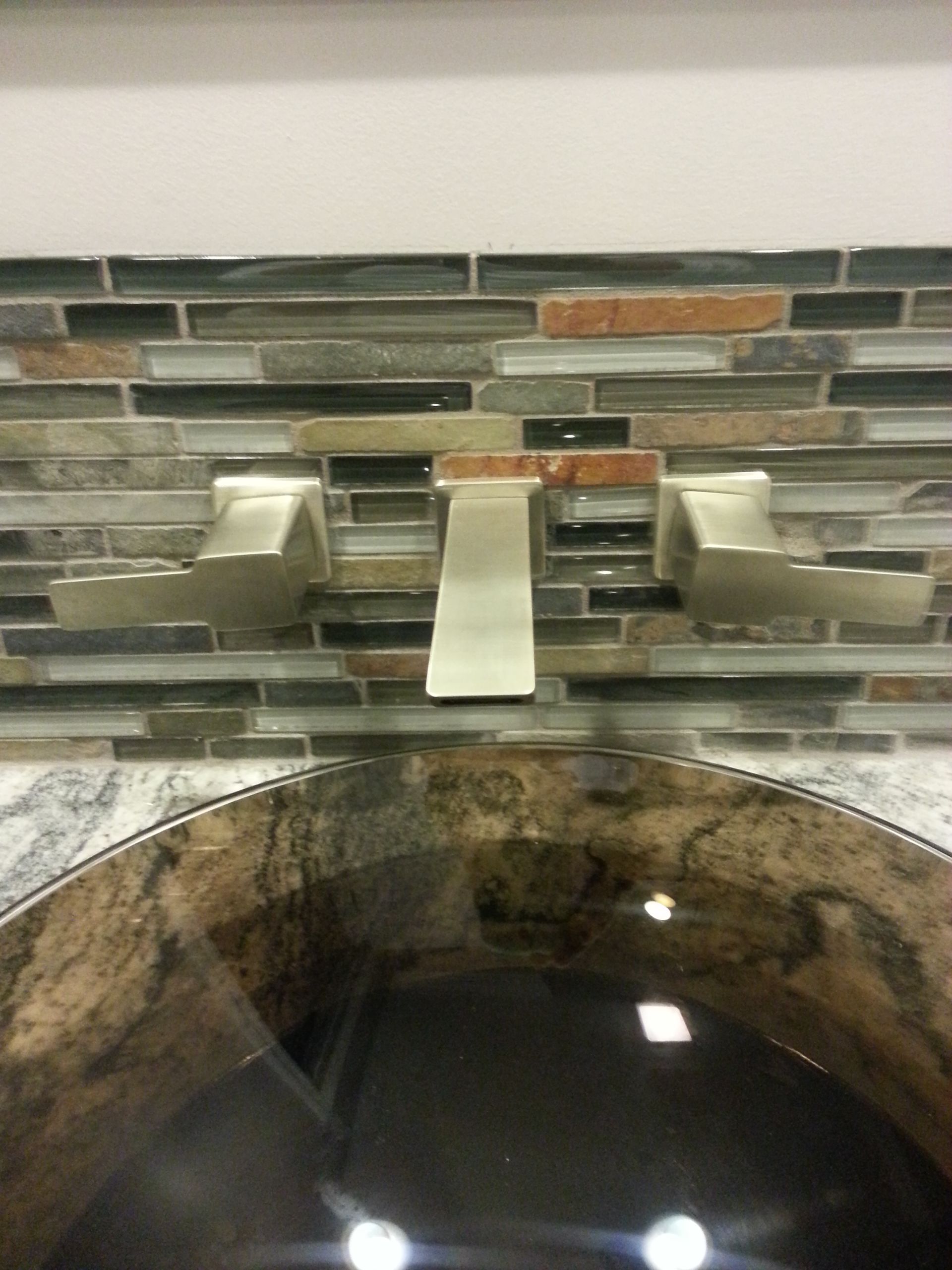 A bathroom sink with a faucet and a tiled wall behind it.