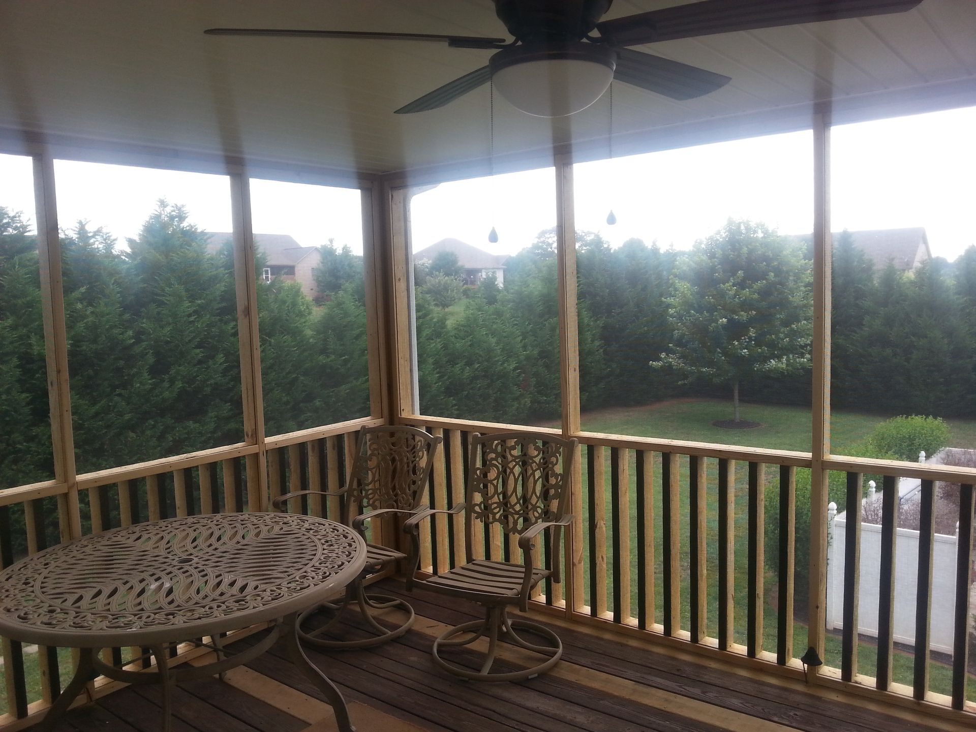 A screened in porch with a table and chairs and a ceiling fan