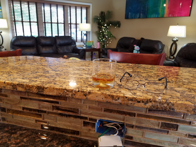 A glass of whiskey sits on a counter in a living room.