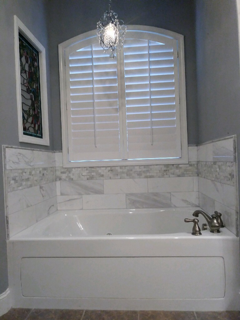 A bathroom with a bathtub and a window with shutters.