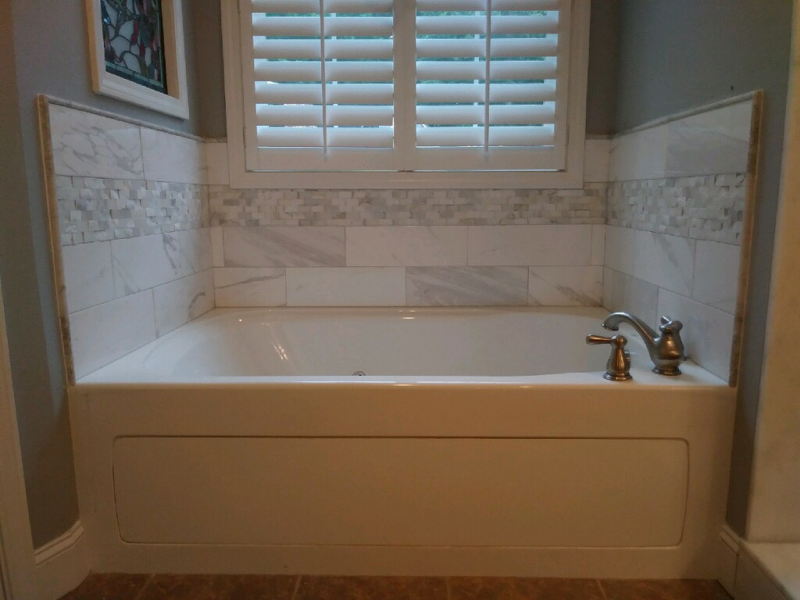 A bathtub in a bathroom next to a window with shutters.