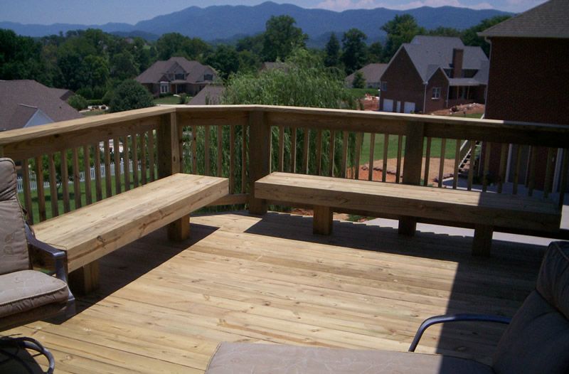 A wooden deck with a bench and chairs and mountains in the background
